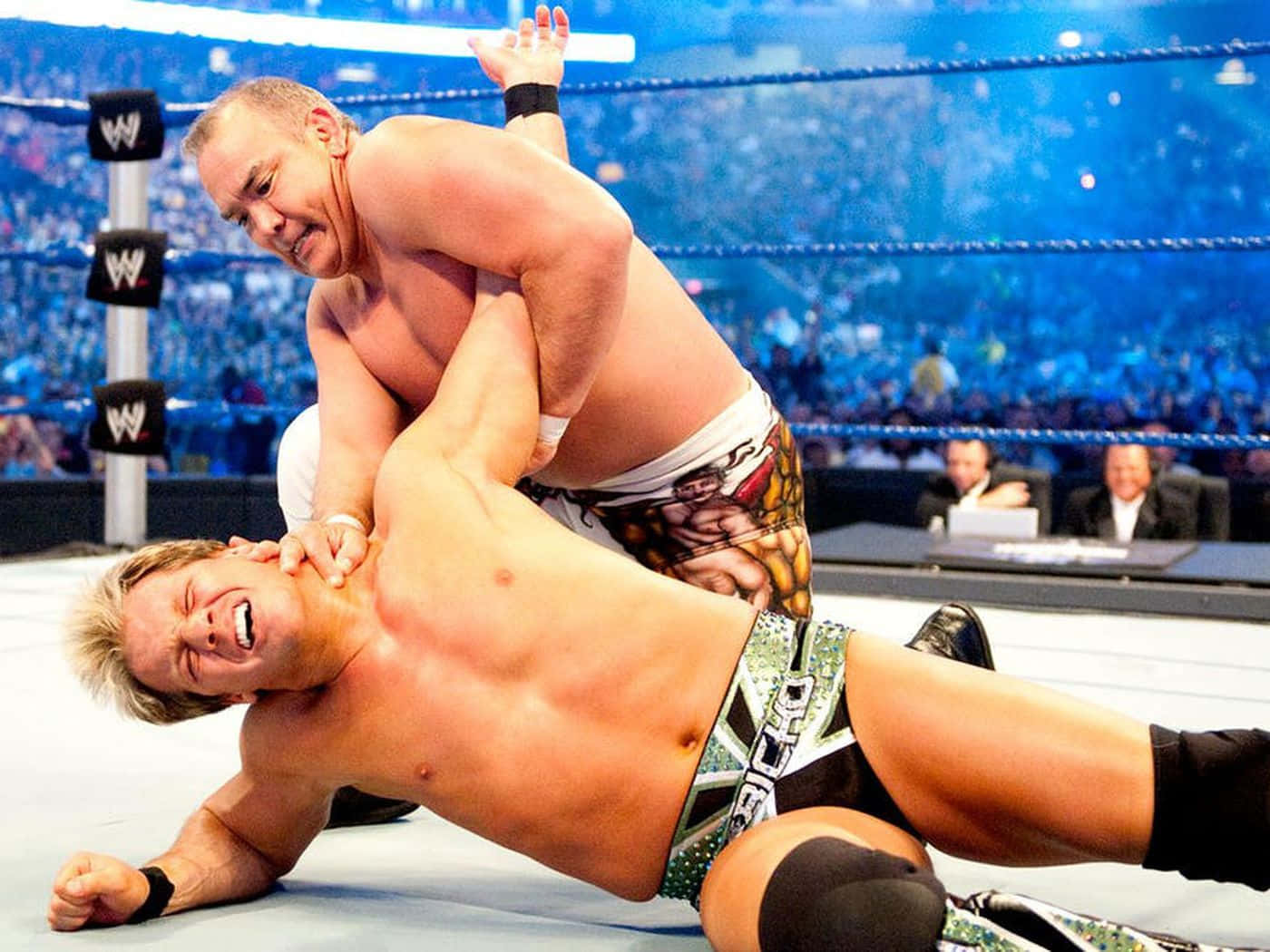 WWE 桌布 壁紙 — 兩名肌肉發達的摔角手在燈火通明的擂台上激烈纏鬥，背景是喧囂的人群。
