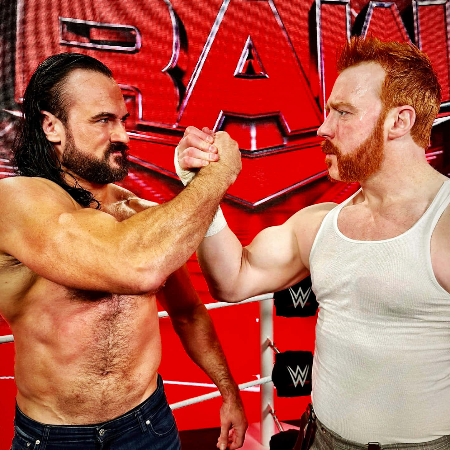 WWE 桌布 壁紙 — 兩名肌肉發達的摔角手在紅色「RAW」背景的WWE擂台上進行緊張的掰手腕比賽。