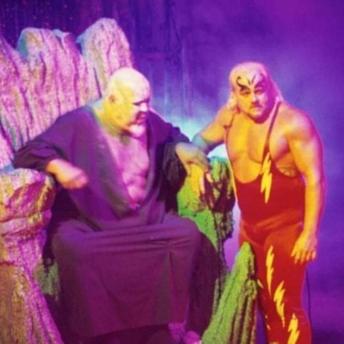 WWE 桌布 壁紙 — 兩名肌肉發達的摔角手穿著鮮豔的服裝，在戲劇性的燈光下，以紫色岩石背景為襯托，擺出戲劇性的姿勢。