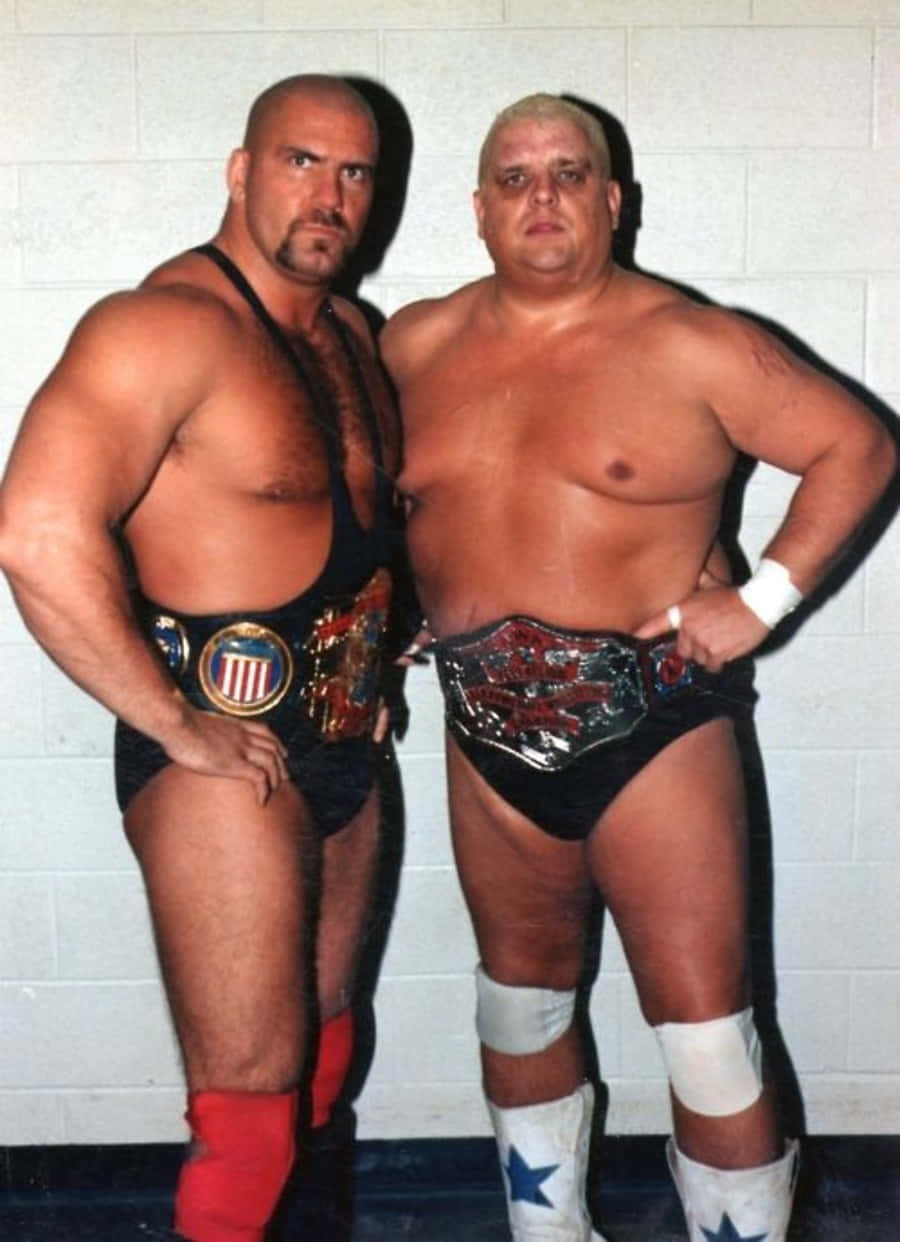 Dusty Rhodes 桌布 壁紙 — 兩名肌肉發達的摔角手自信地擺姿勢，背景是白色煤渣磚牆，每人佩戴冠軍腰帶和摔角短褲。