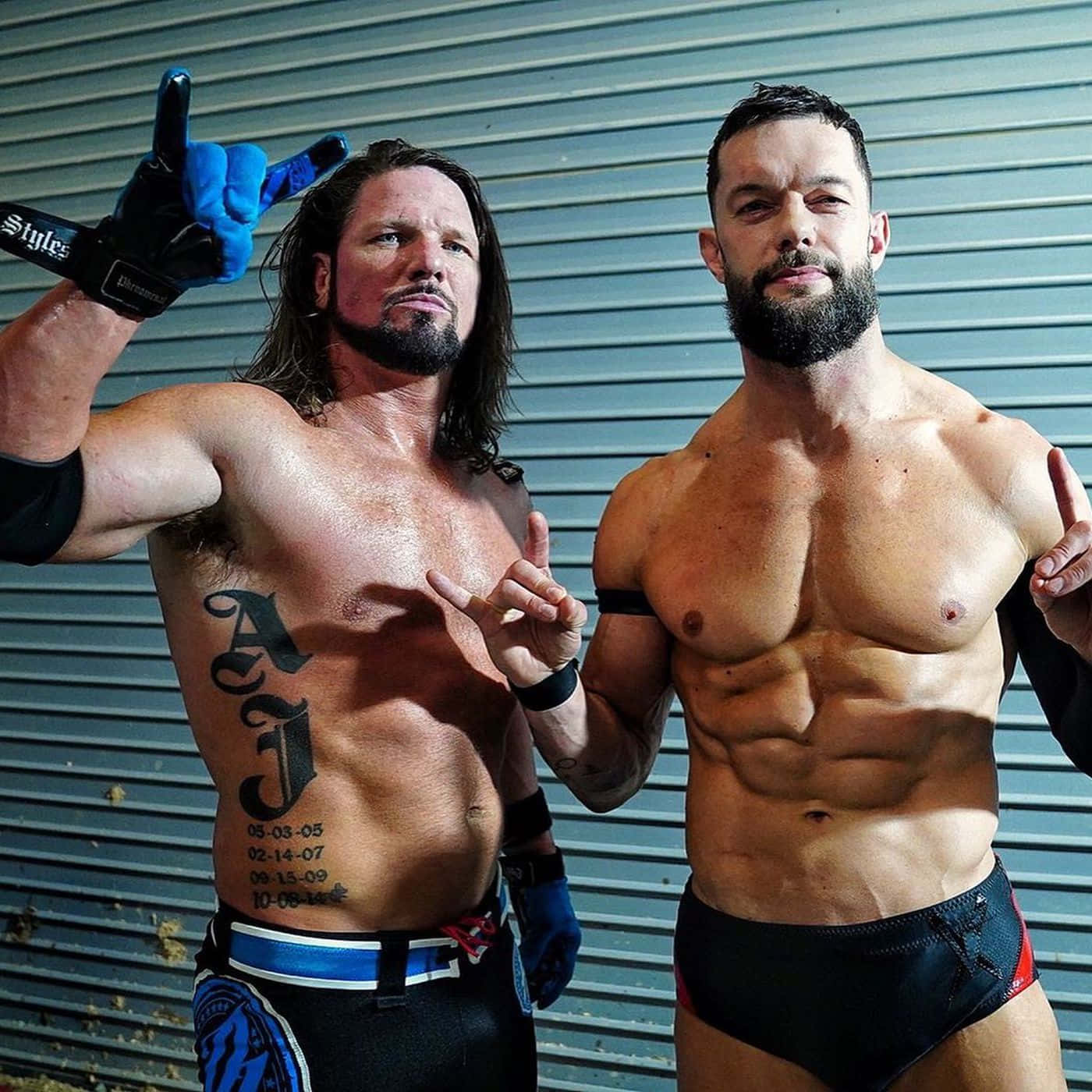 WWE 桌布 壁紙 — 兩名肌肉發達的摔角手自信地靠在波紋金屬牆上，身上有刺青並穿著摔角裝備。