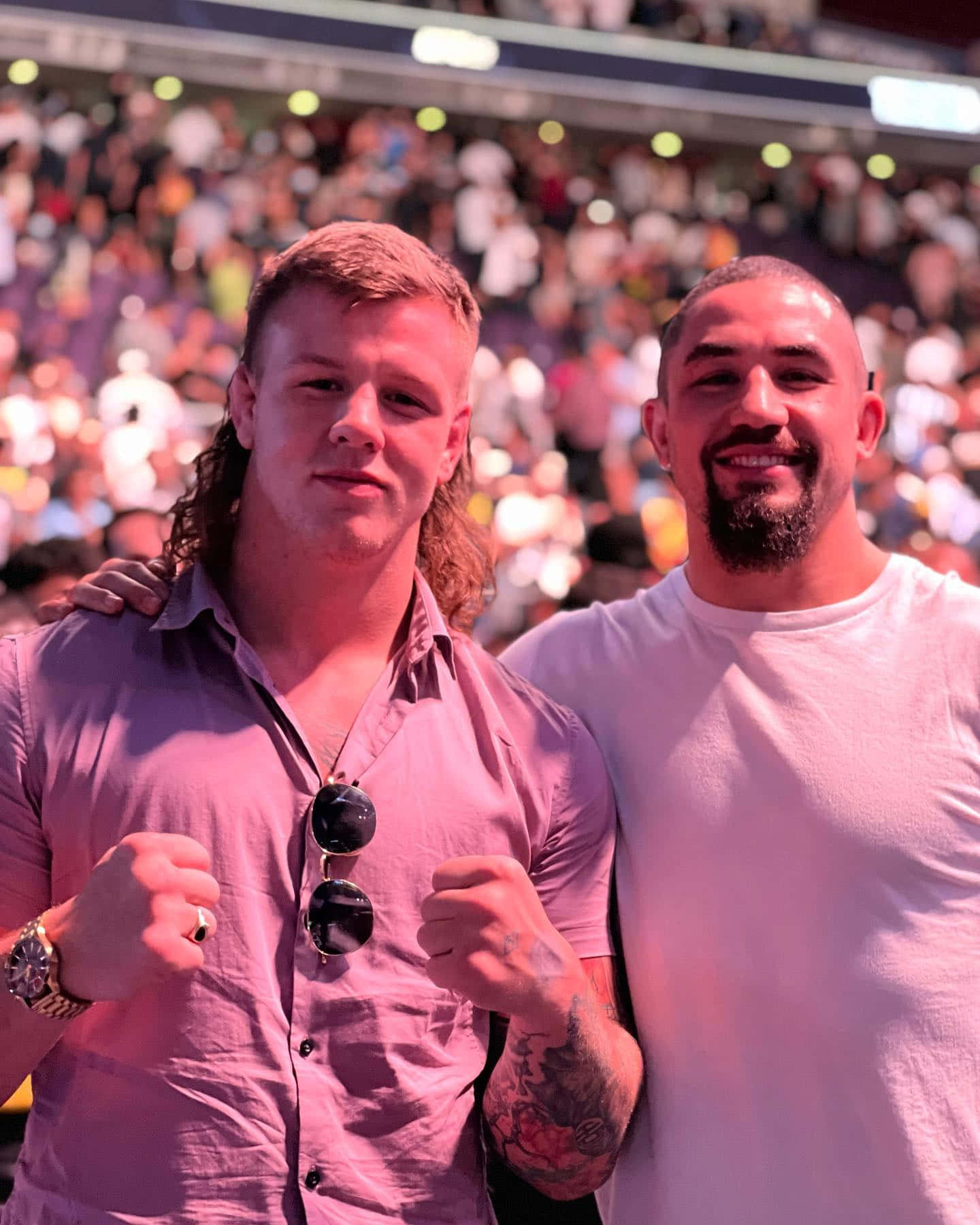 UFC 桌布 壁紙 — 兩名肌肉發達的男子在陽光明媚的體育館中自信地舉起拳頭，周圍是歡呼的粉絲。