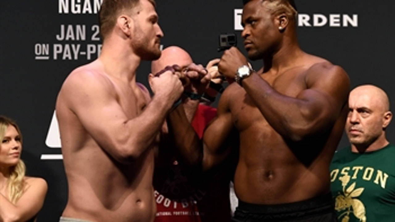 UFC 桌布 壁紙 — 兩名肌肉發達的男性拳手在緊張的賽前稱重中對峙，相機閃光燈閃爍，工作人員在附近。