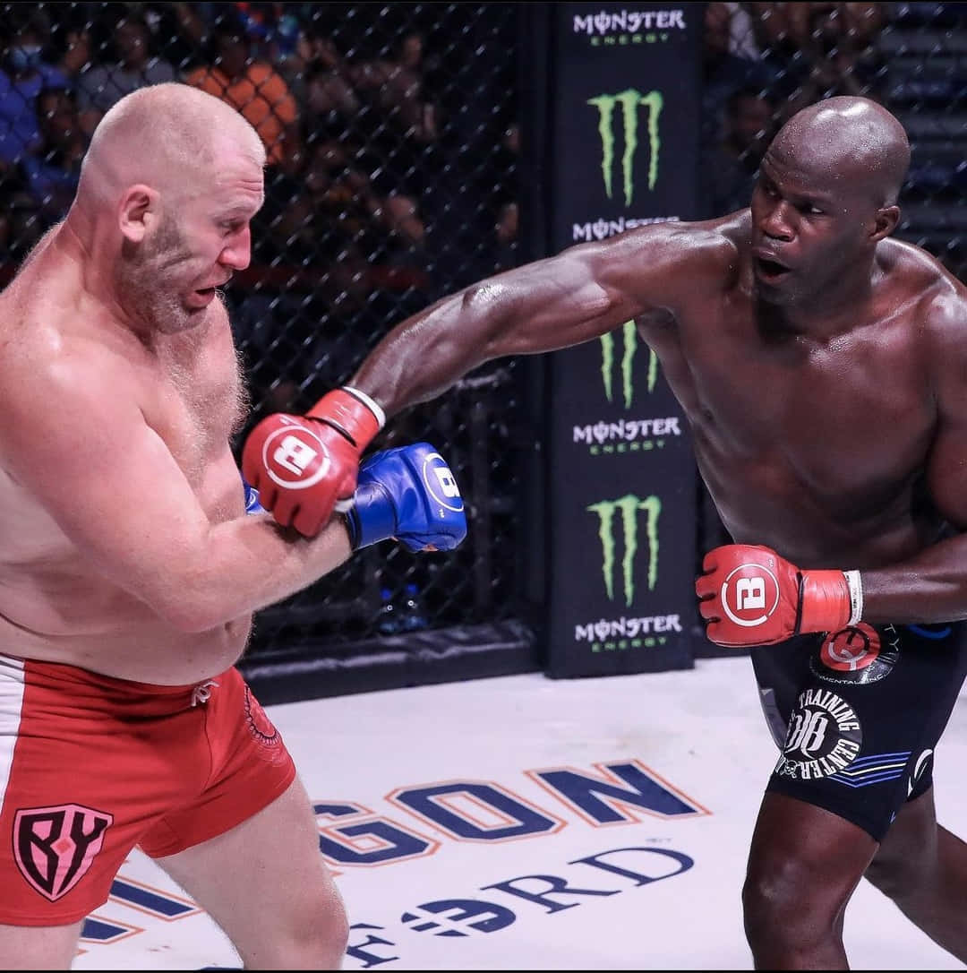 MMA 桌布 壁紙 — 兩名肌肉發達的鬥士在籠中激烈交鋒，其中一人揮拳，觀眾緊張注視。