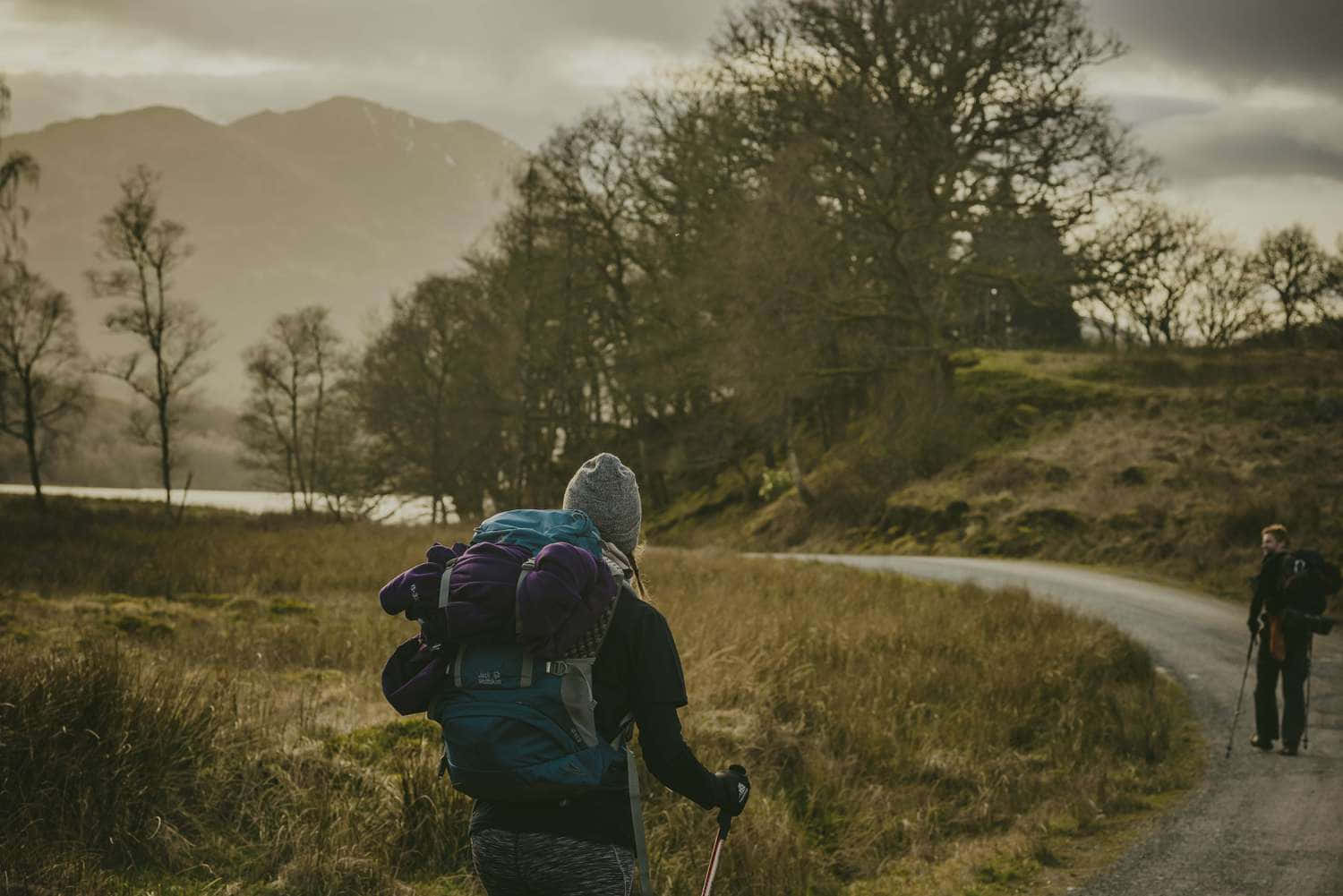 Hiking 桌布 壁紙 — 兩名背著大型背包的遠足者沿著蜿蜒的泥土小徑穿過黎明時分霧氣瀰漫的山區景觀。