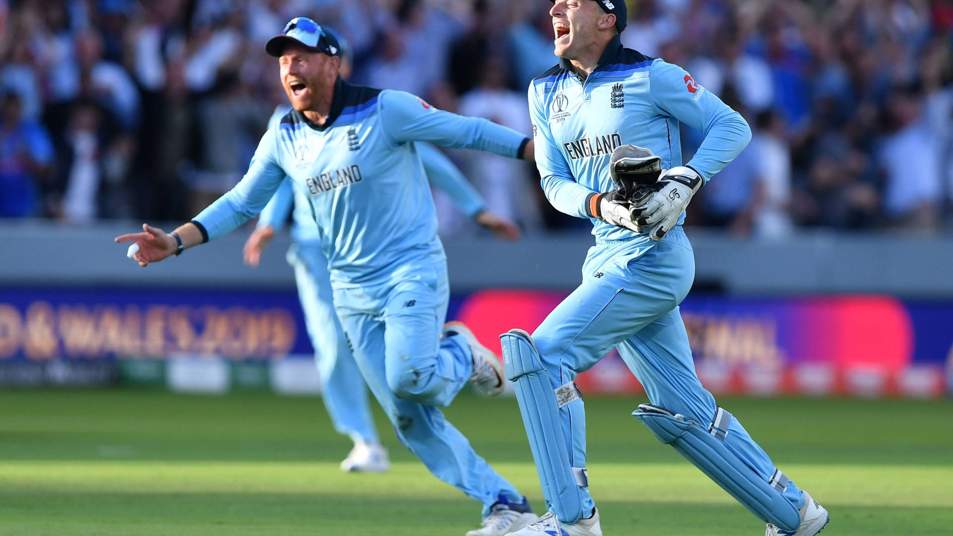 jos buttler 桌布 壁紙 — 兩名英格蘭板球球員身穿淺藍色球衣，在陽光明媚的綠色球場上熱情慶祝，背景是歡呼的人群。