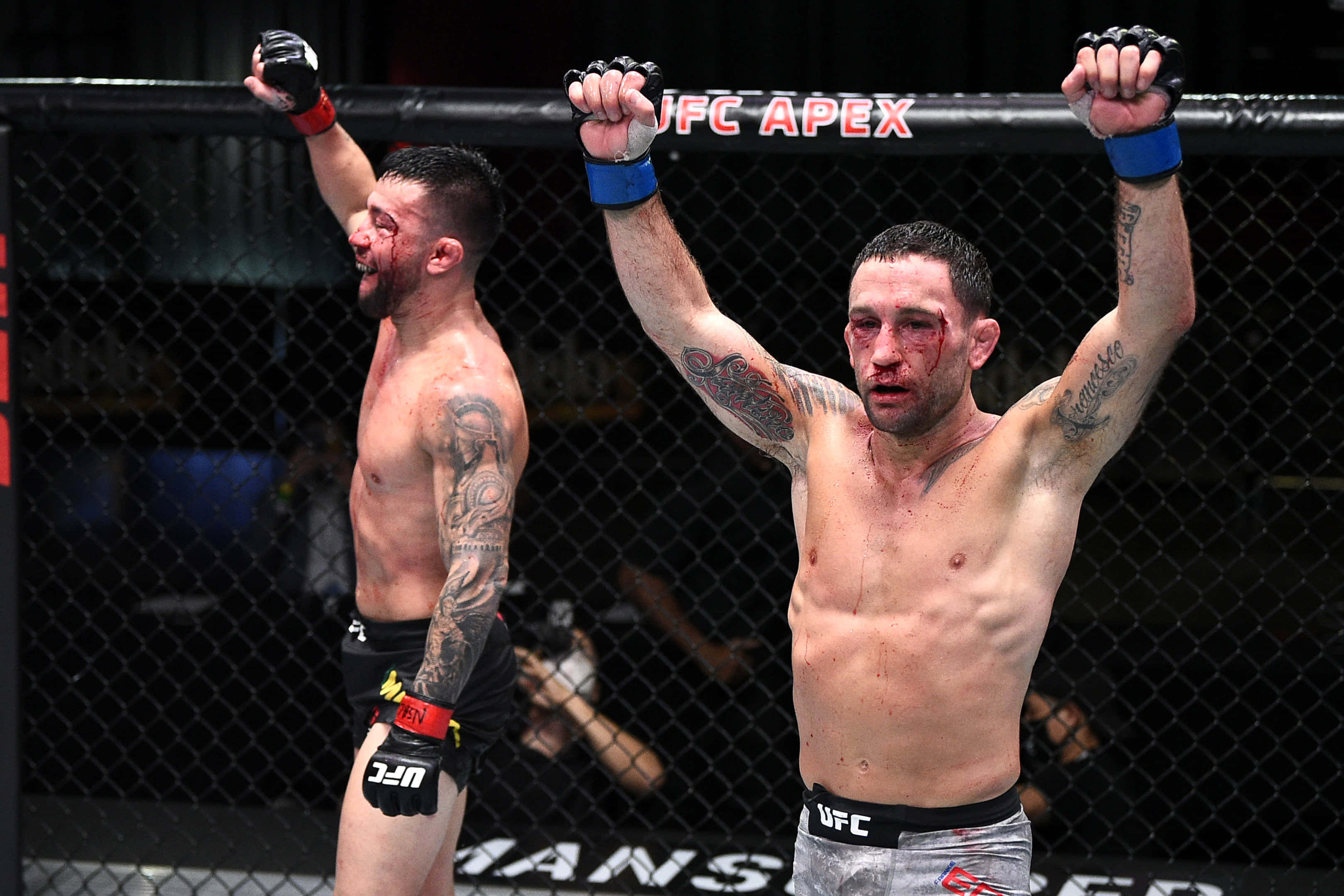 UFC 桌布 壁紙 — 兩名血跡斑斑的MMA拳手在UFC八角籠內舉起手臂慶祝勝利，上方可見「UFC APEX」。