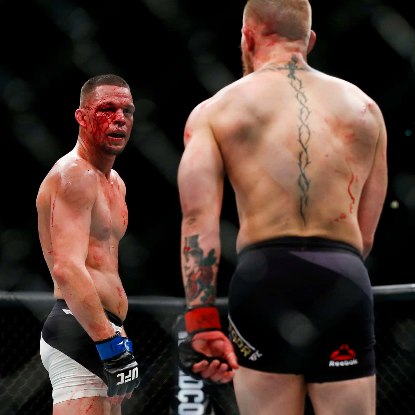 UFC 桌布 壁紙 — 兩名血跡斑斑的MMA拳手在八角籠內對峙，一人背部有明顯刺青，另一人臉上帶血。