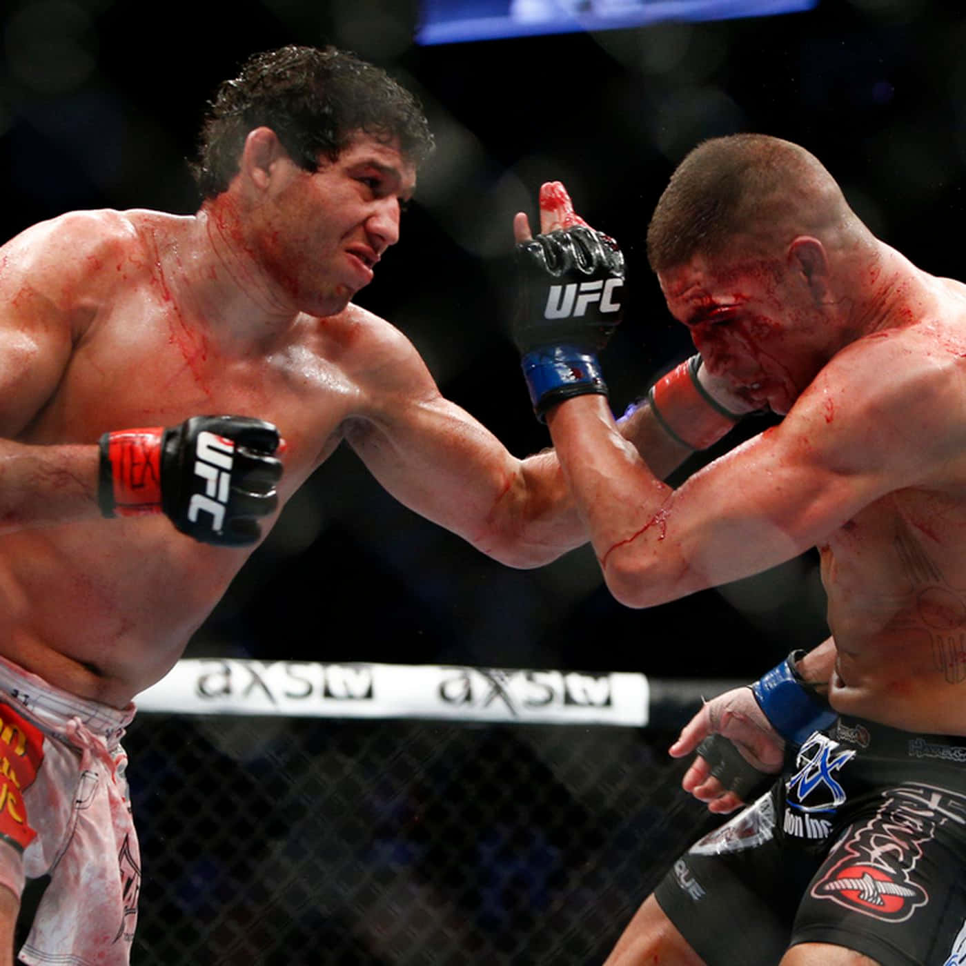 UFC 桌布 壁紙 — 兩名血跡斑斑的MMA拳手在明亮的場館燈光下進行激烈的籠中對決。
