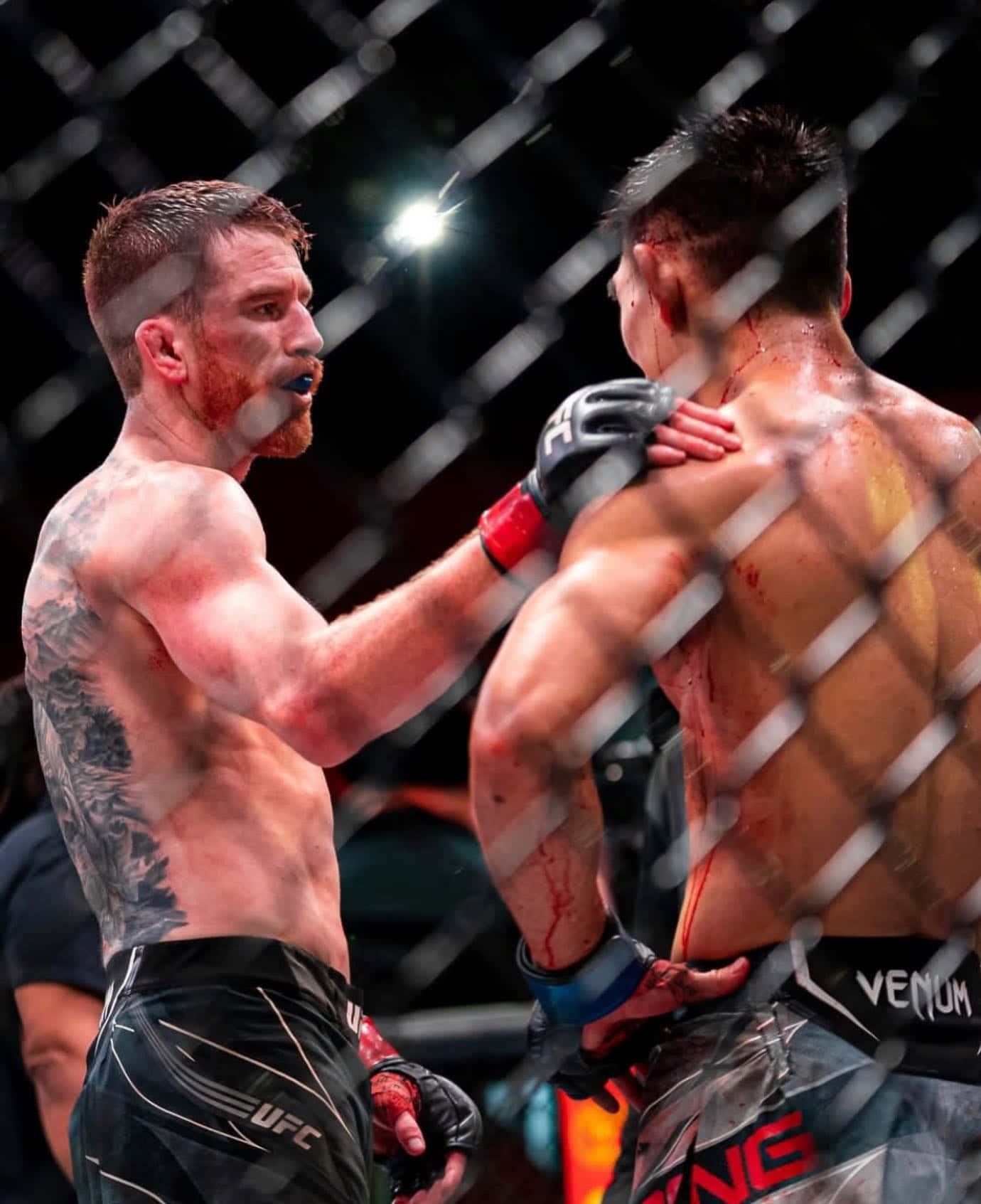 MMA 桌布 壁紙 — 兩名血跡斑斑的MMA拳手在明亮的場館燈光下於八角籠內對峙。