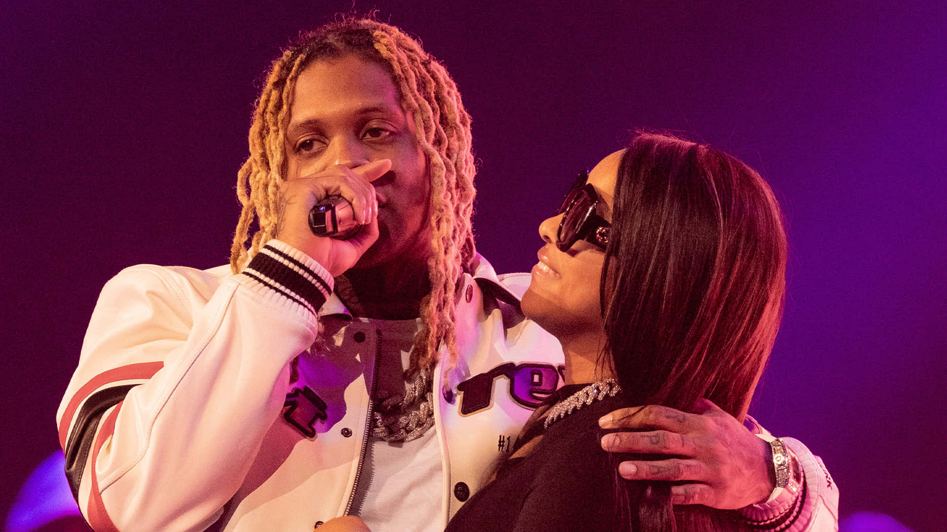 Lil Durk 桌布 壁紙 — 兩名表演者在紫色燈光下的舞台上，一人手持麥克風，另一人戴著太陽眼鏡微笑。