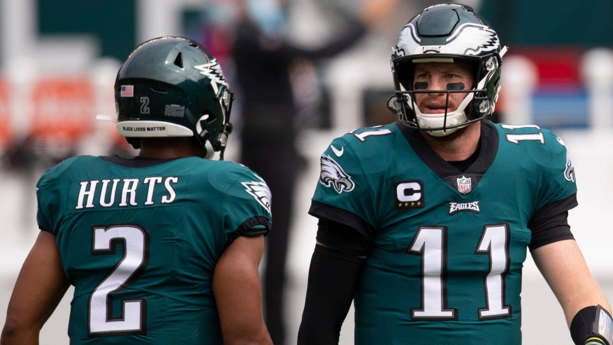 Jalen Hurts Eagles 桌布 壁紙 — 兩名費城老鷹隊美式足球員身穿藍綠色球衣在比賽期間於場上交談。
