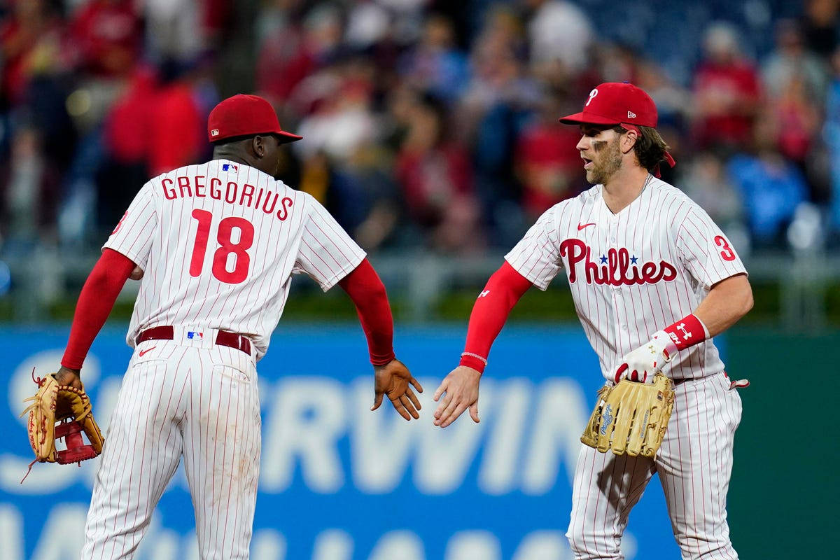 Phillies 桌布 壁紙 — 兩名費城費城人棒球運動員身穿細條紋制服，在陽光明媚的球場上擊掌，背景是模糊的球迷。