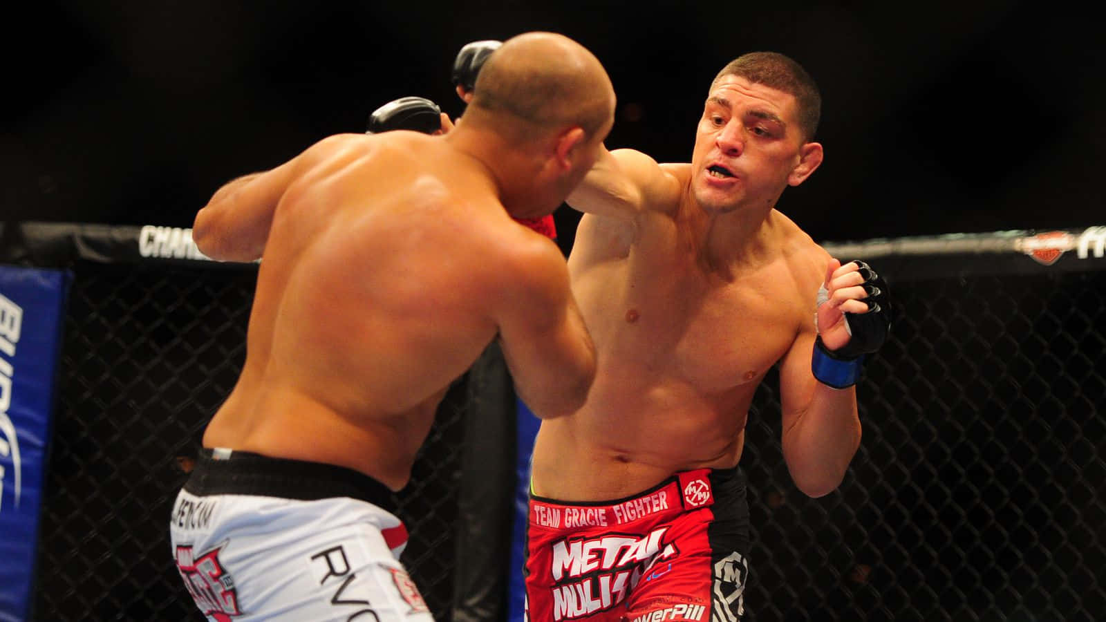 UFC 桌布 壁紙 — 兩名赤膊拳手在燈光昏暗、帶有鐵絲網圍欄的MMA八角籠內互相揮拳。
