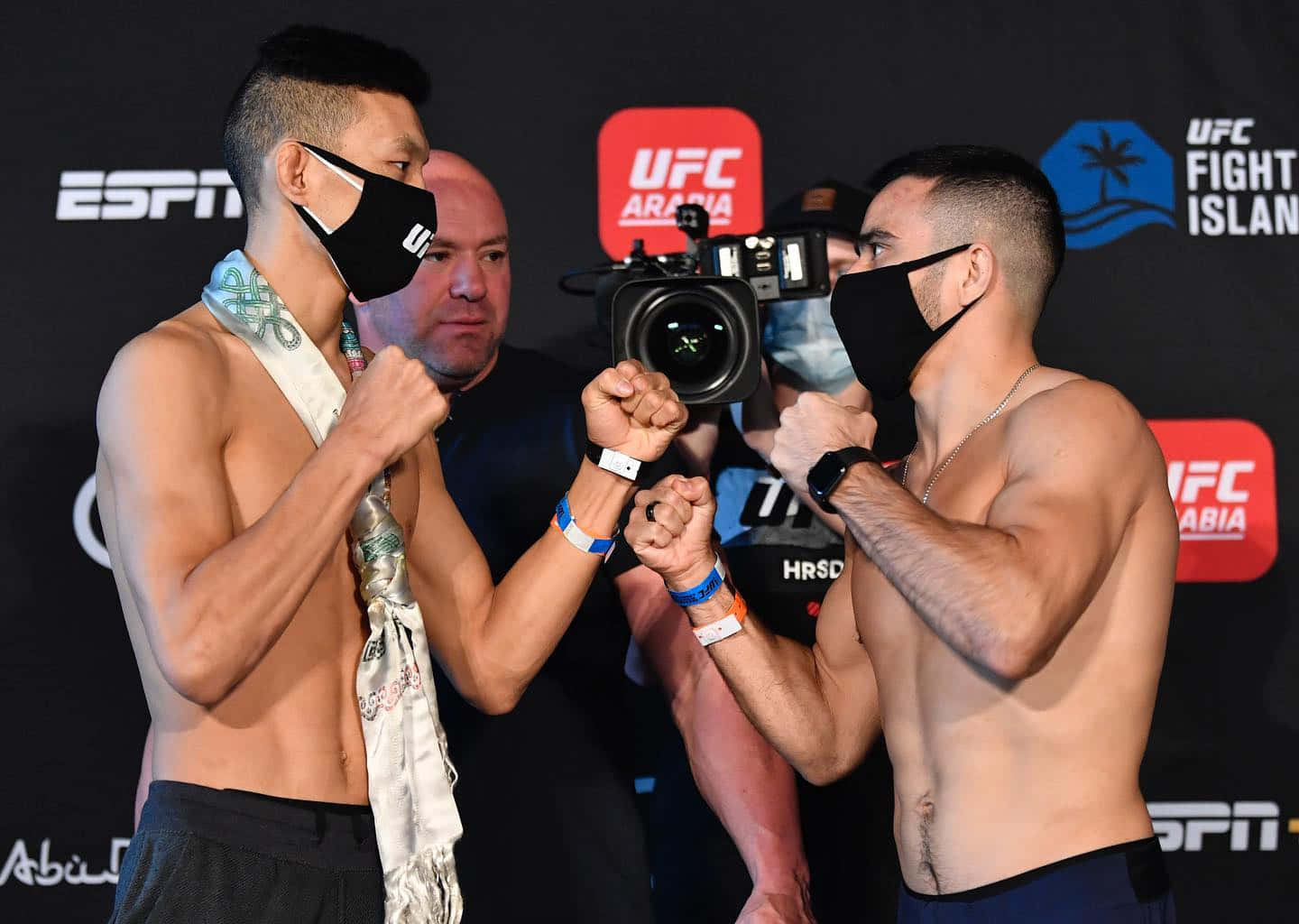 UFC 桌布 壁紙 — 兩名赤裸上身、戴黑色口罩的UFC拳手在稱重活動中緊握拳頭，進行緊張的賽前對峙。
