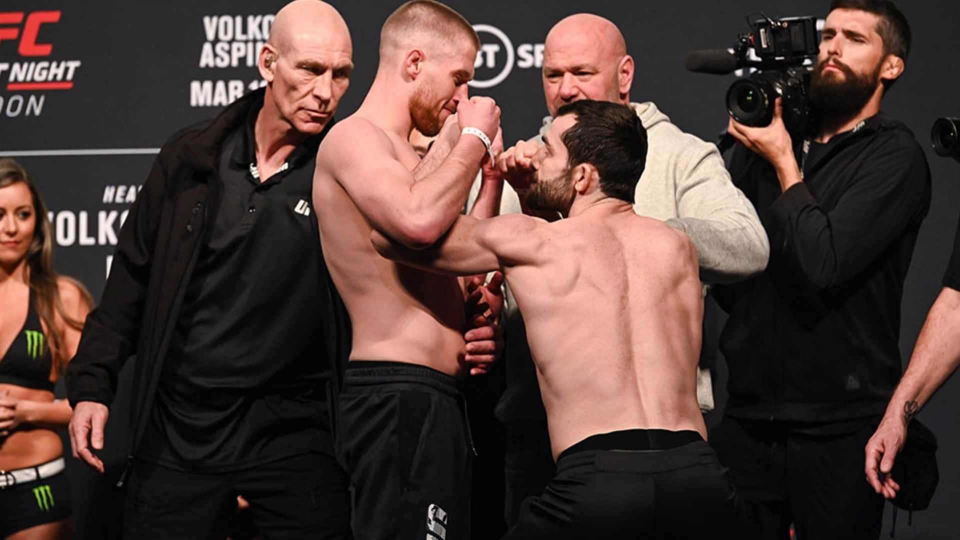 UFC 桌布 壁紙 — 兩名赤裸上身的MMA拳手在UFC賽事中，在官員和攝影機的包圍下，進行緊張的賽前對峙。