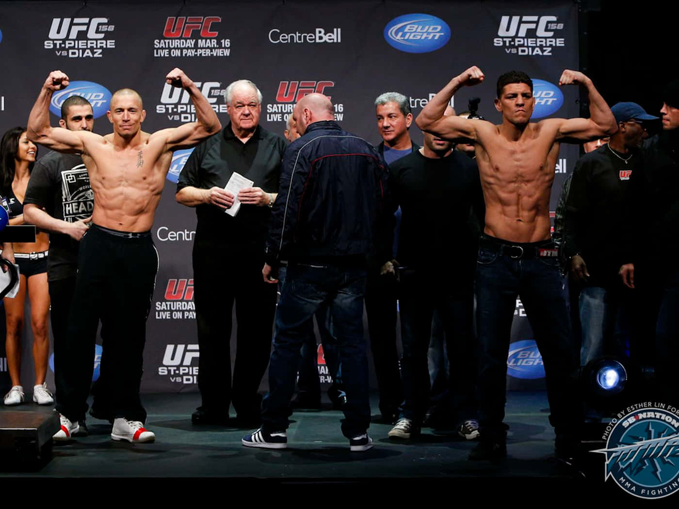 UFC 桌布 壁紙 — 兩名赤裸上身的UFC拳手在明亮的舞台燈光下，於有品牌背景的稱重活動中展示肌肉。