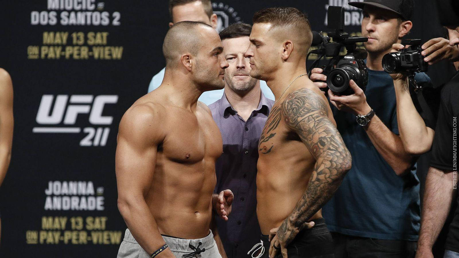 UFC 桌布 壁紙 — 兩名赤裸上身的UFC拳手在磅重時激烈對峙，周圍閃光燈不斷。