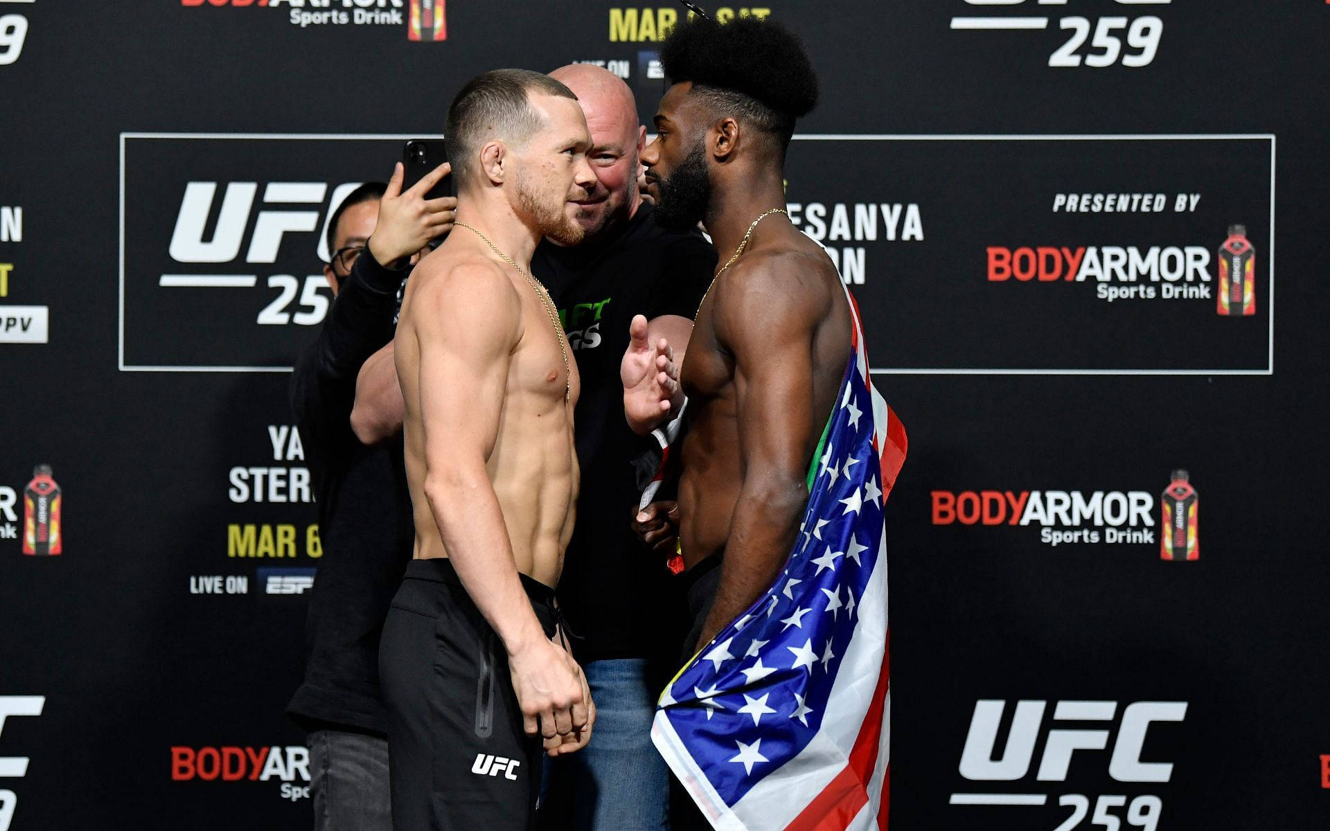 Petr Yan 桌布 壁紙 — 兩名赤裸上身的UFC拳手在稱重儀式上對峙，其中一人披著美國國旗，背景有品牌標誌。