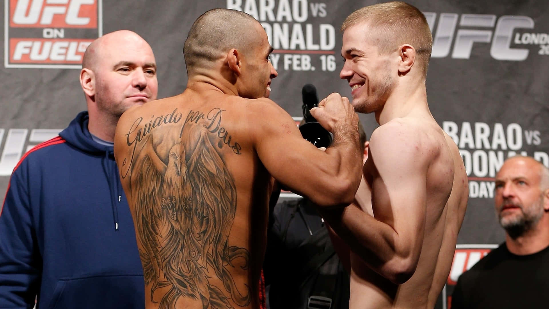 UFC 桌布 壁紙 — 兩名赤裸上身的UFC拳手在稱重時對峙，其中一人背部展示了一個大型天使翼刺青。
