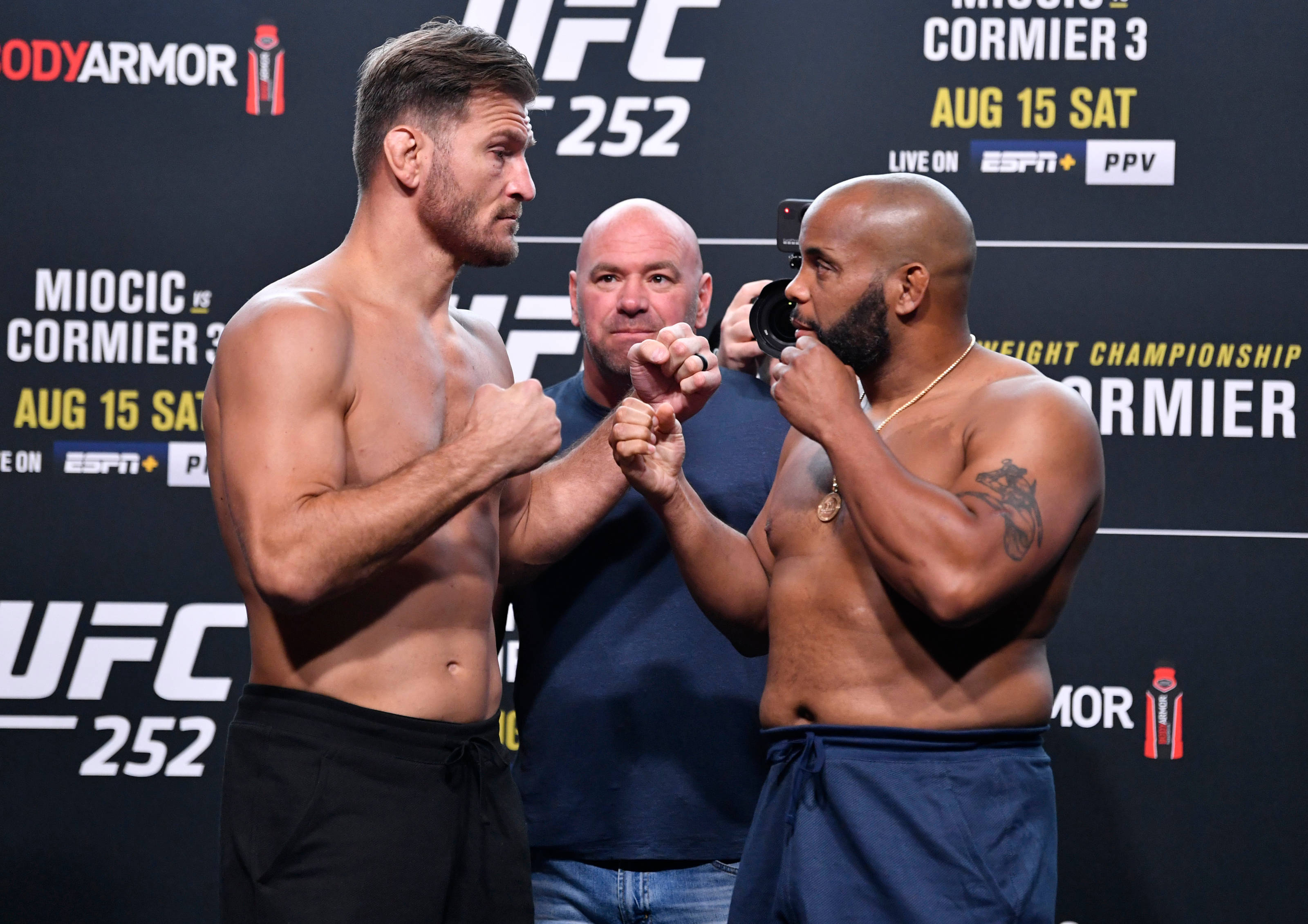UFC 桌布 壁紙 — 兩名赤裸上身的UFC拳手在稱重活動中與裁判和品牌背景緊張地鎖拳對視。