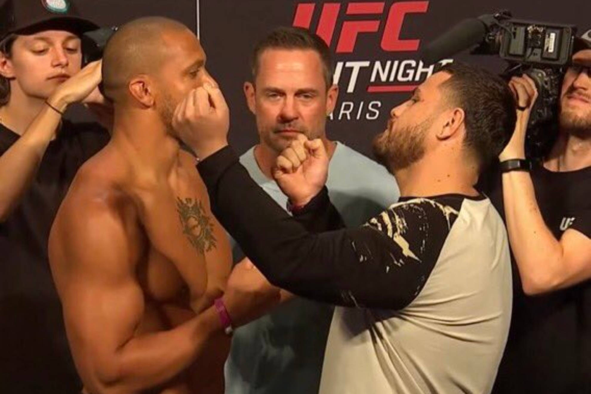 MMA 桌布 壁紙 — 兩名赤裸上身的UFC拳手在緊張的賽前對峙中面對面，周圍有攝影機和工作人員。