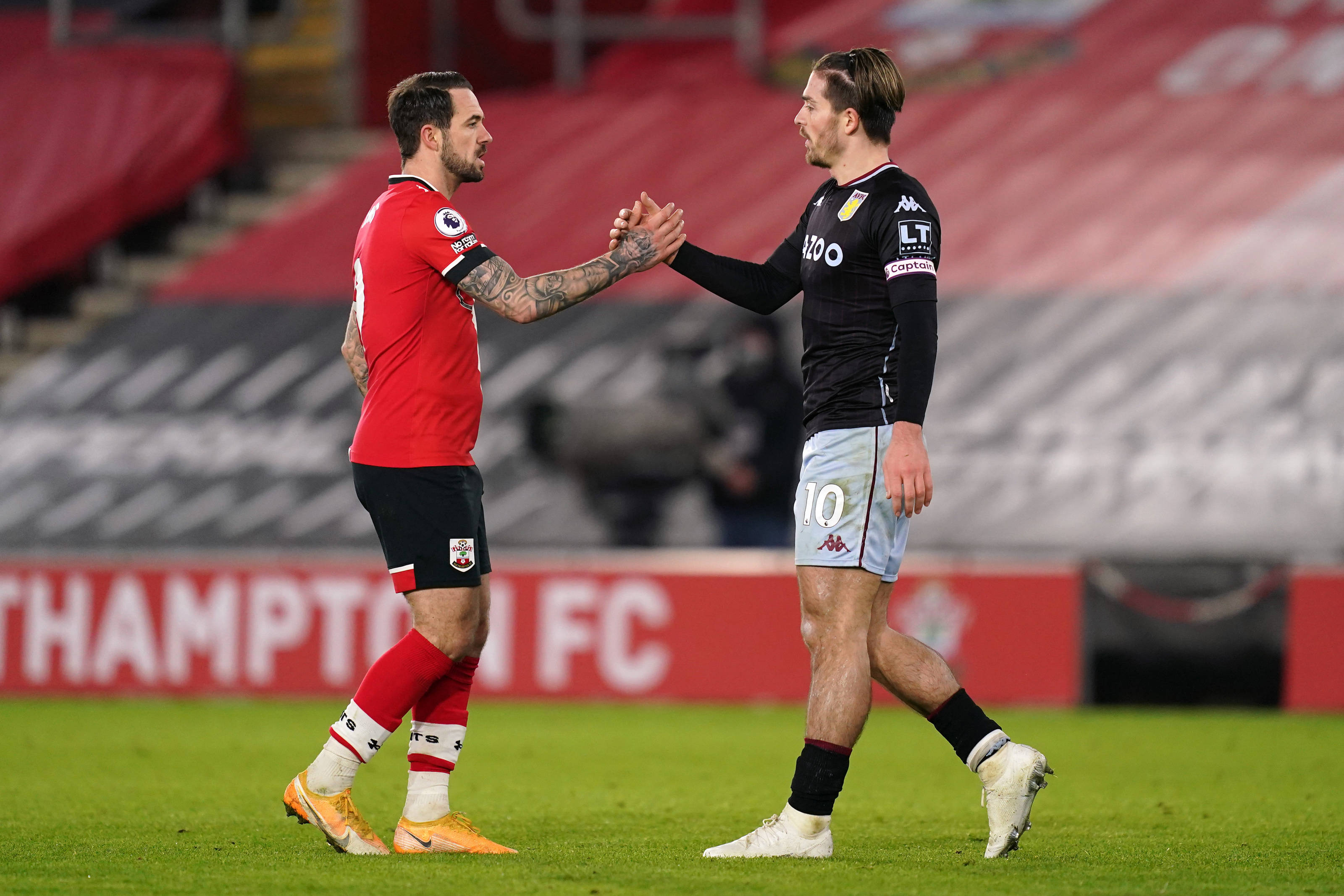 Football Players 桌布 壁紙 — 兩名足球運動員在一個有紅色座位和「SOUTHAMPTON FC」標誌的體育場草地上握手。