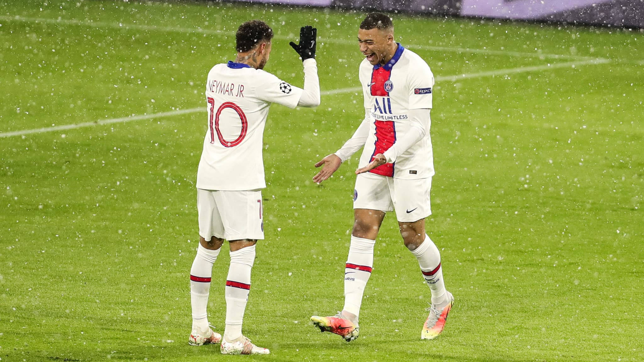 Football Players 桌布 壁紙 — 兩名足球運動員在球場燈光下於濕滑的雨地球場慶祝進球。