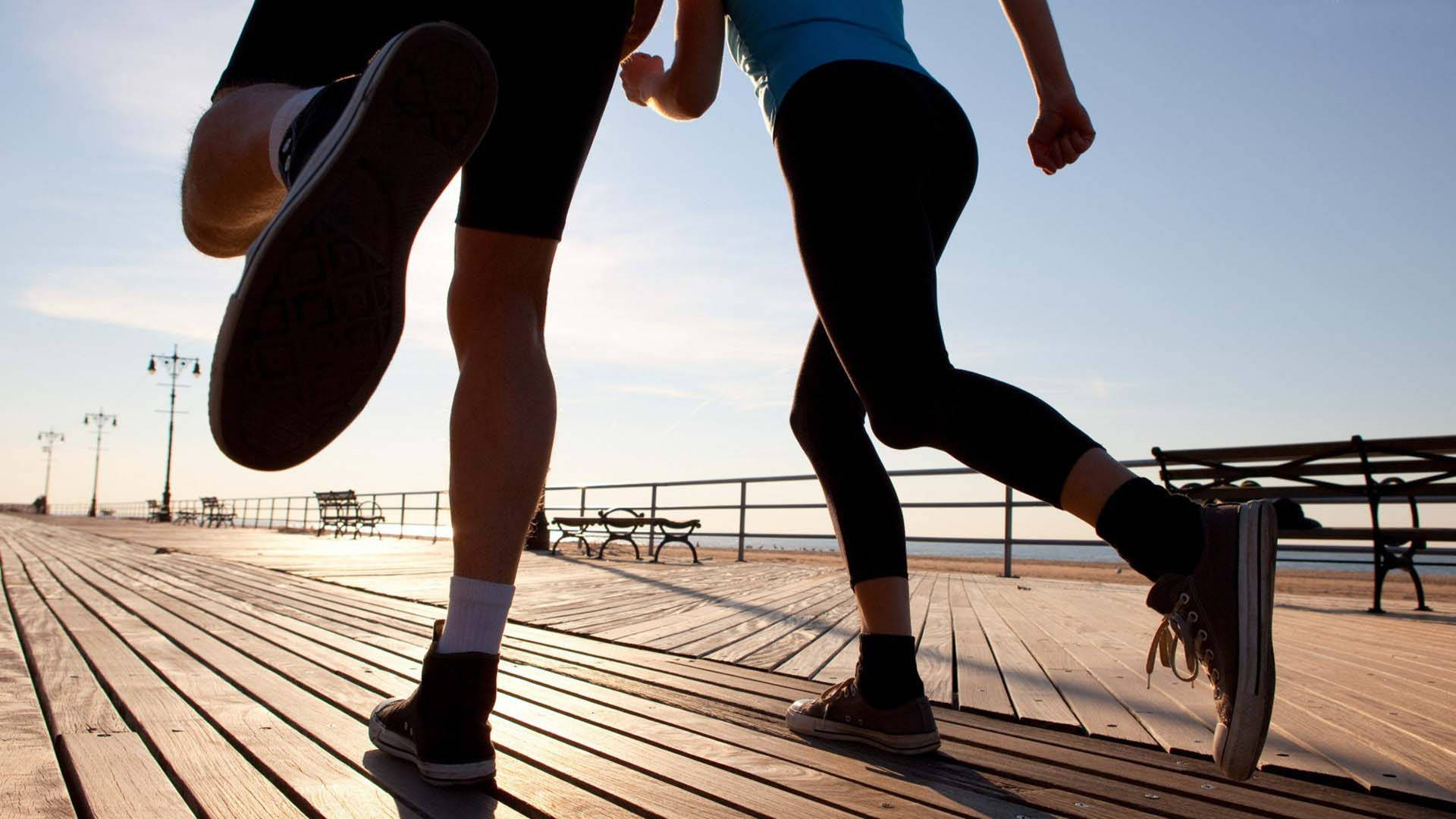 Exercise 桌布 壁紙 — 兩名跑者在黃金時段於木製步道上邁步前進，背景是海景和路燈。