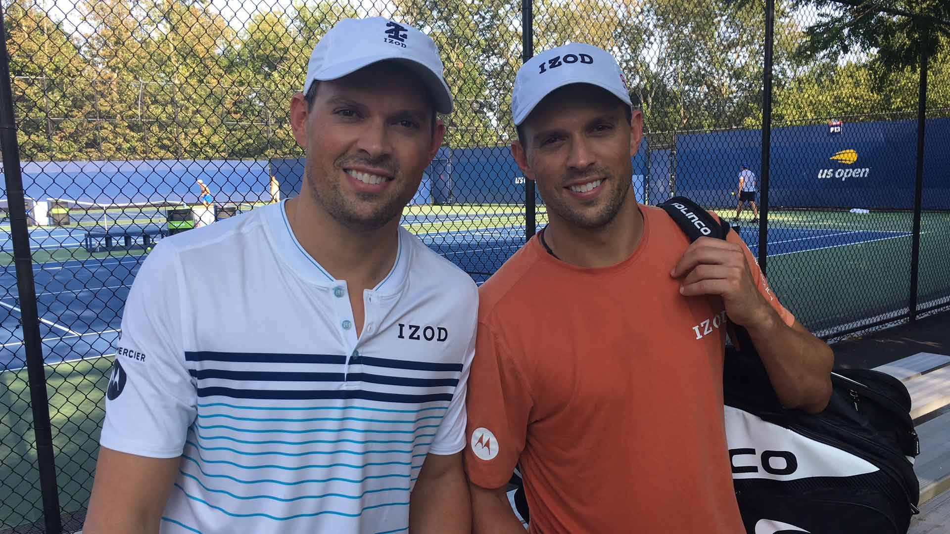 Athlete 桌布 壁紙 — 兩名身穿 Izod 裝備的網球選手面帶微笑，在藍色硬地球場上一起擺姿勢，背景有鐵絲網圍欄和樹木。