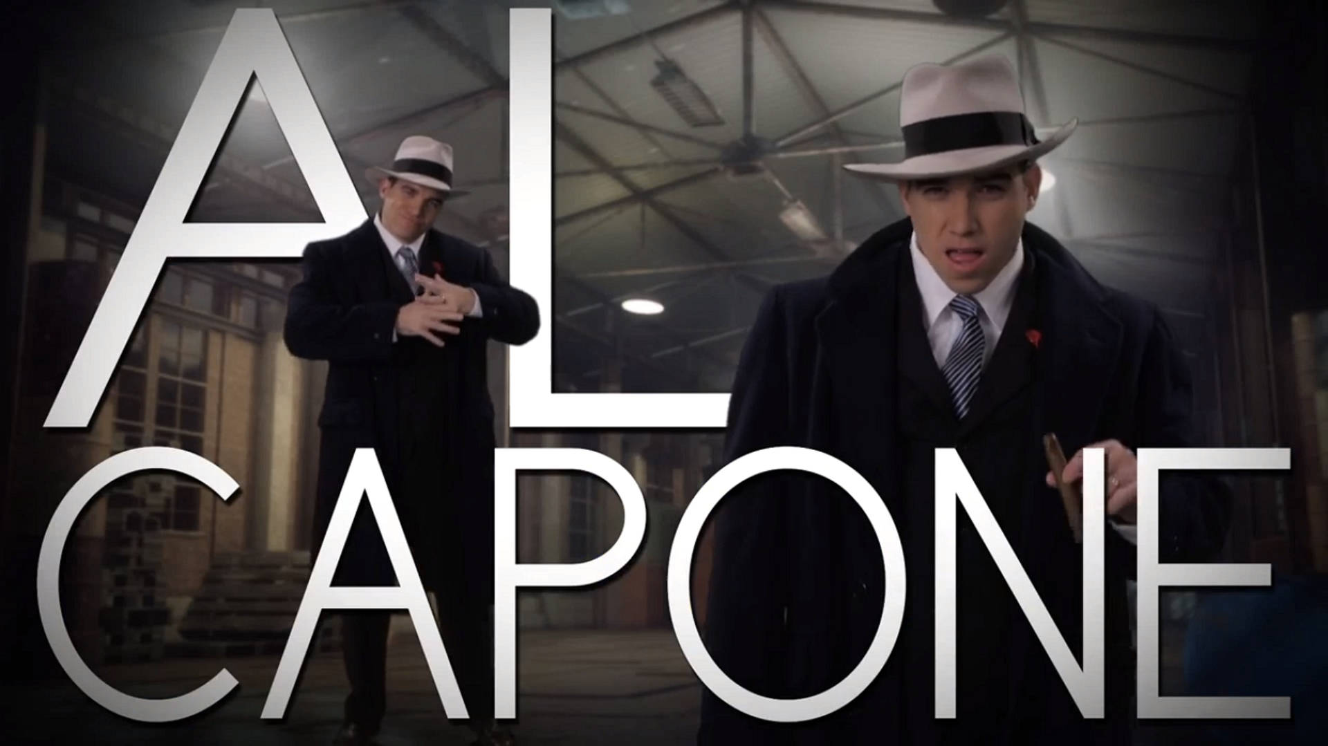 Capone 桌布 壁紙 — 兩名身穿1920年代西裝和軟呢帽的男子站在光線昏暗的工業空間中，帶有大型「AL CAPONE」文字疊加。