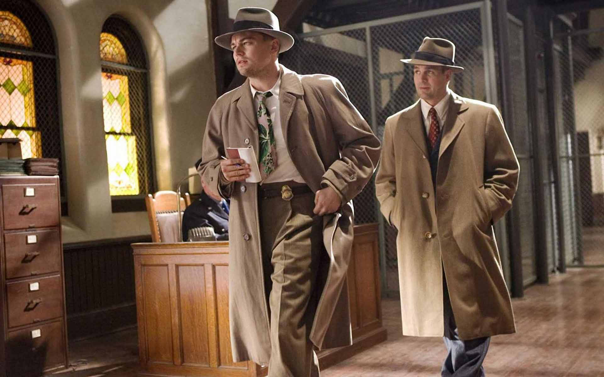 Hollywood Movie 桌布 壁紙 — 兩名身穿1940年代偵探大衣和軟呢帽的男子走過一間光線昏暗、帶有彩繪玻璃窗的警察局。