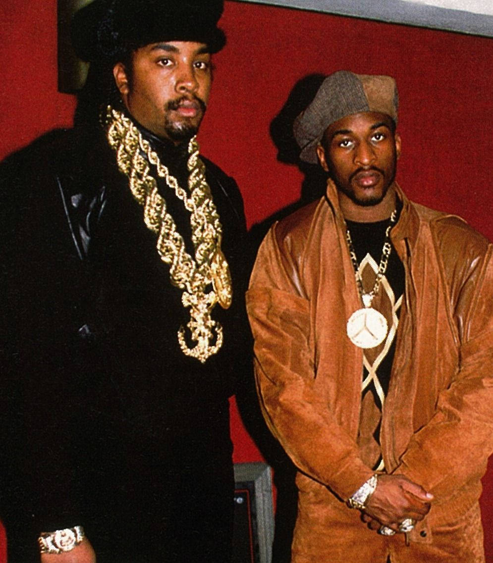Rappers 桌布 壁紙 — 兩名身穿90年代嘻哈服飾的男子，在飾有金鏈和平安符號的紅牆前自信地擺姿勢。
