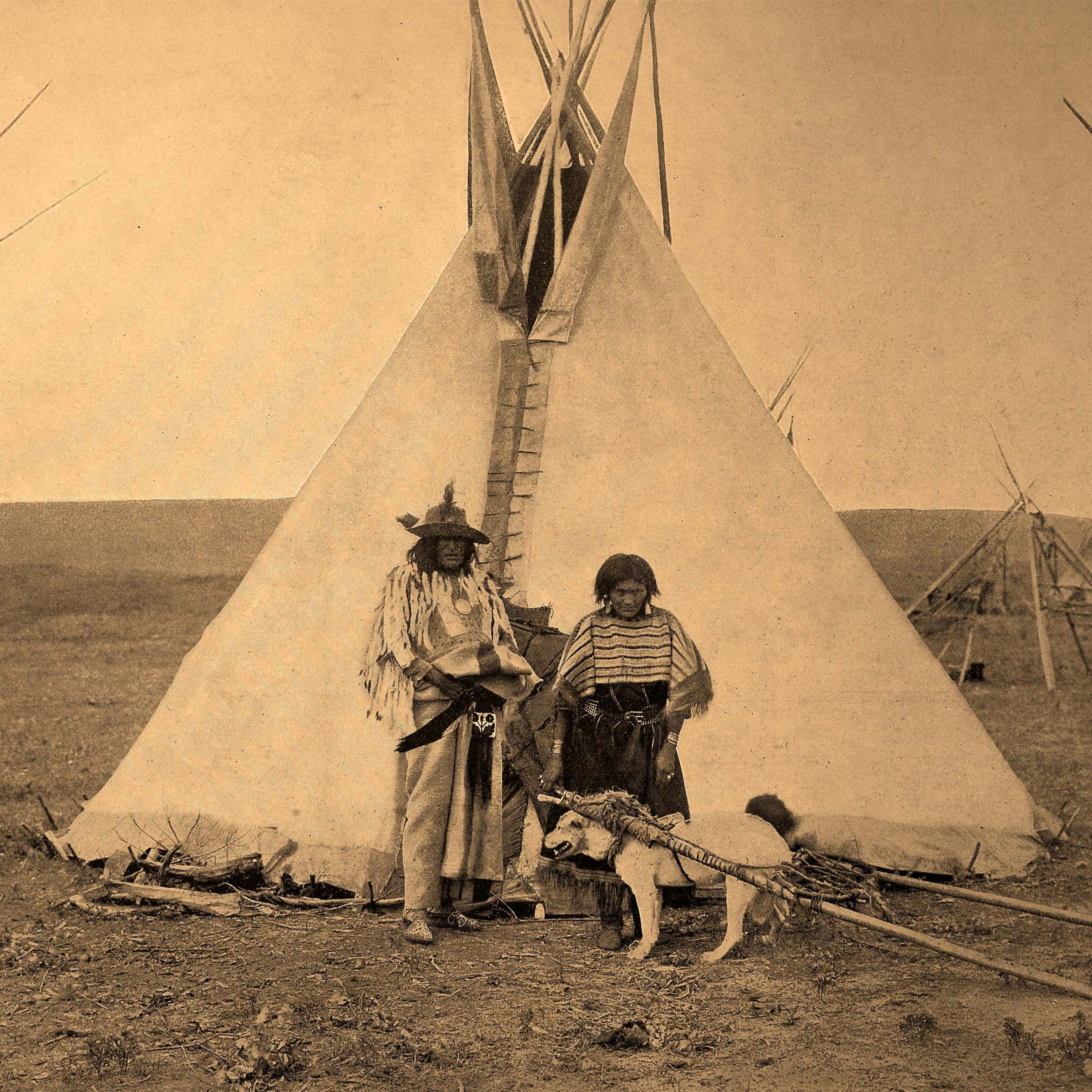 Native American 桌布 壁紙 — 兩名身穿傳統服飾的美國原住民站在一個大型帳篷前，腳邊有一隻狗，身處廣闊的平原。