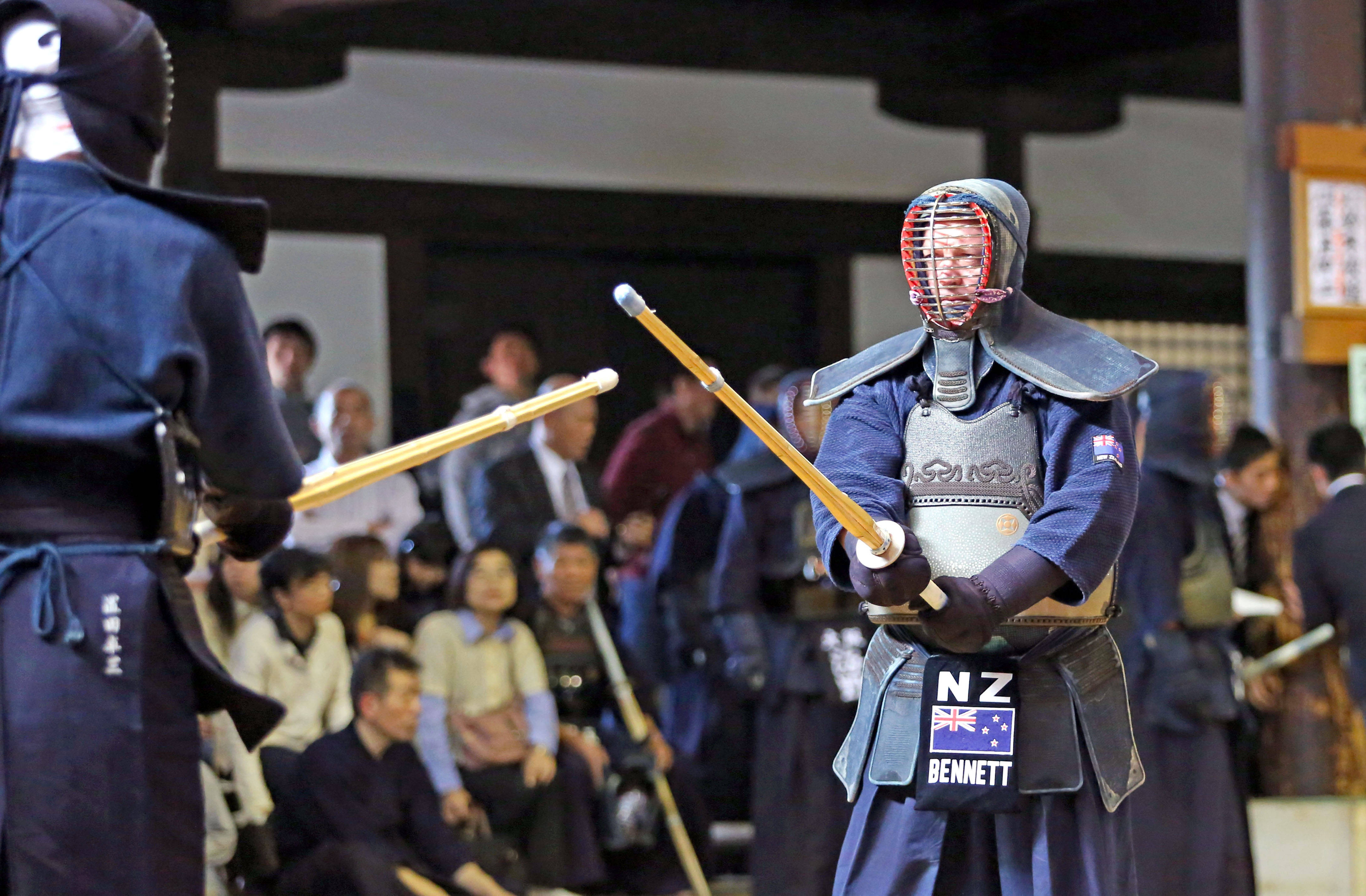 運動 桌布 壁紙 — 兩名身穿全套防護裝備的劍道鬥士在傳統日本建築下以竹劍對峙。