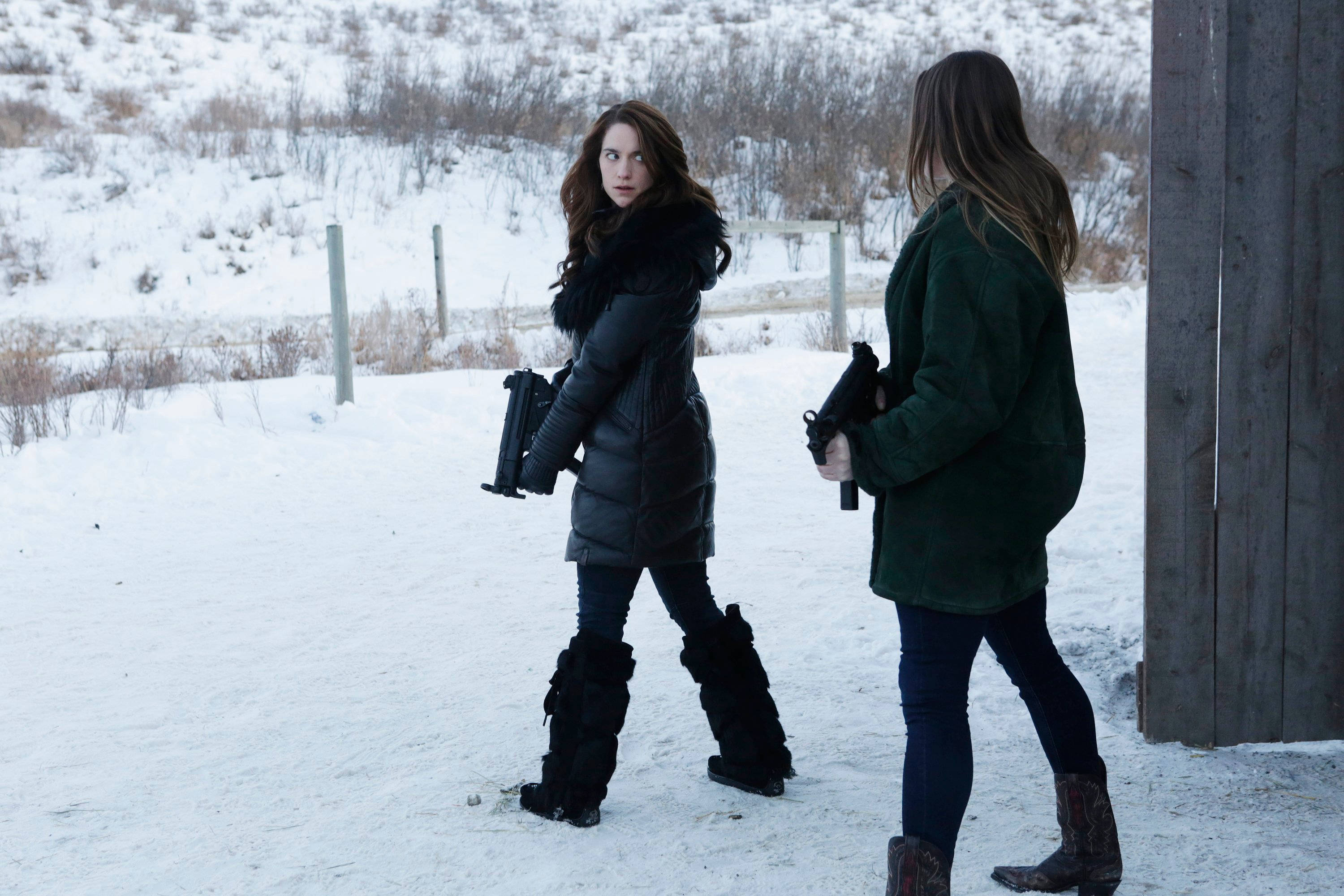 Wynonna Earp 桌布 壁紙 — 兩名身穿冬季外套的女性在雪地中持手槍警覺地站在木結構附近。