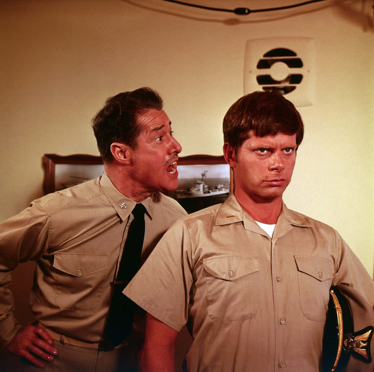 Don Ameche 桌布 壁紙 — 兩名身穿卡其色制服的男人站在一個溫暖光線的房間裡，一個講得很興奮，另一個表情嚴肅。