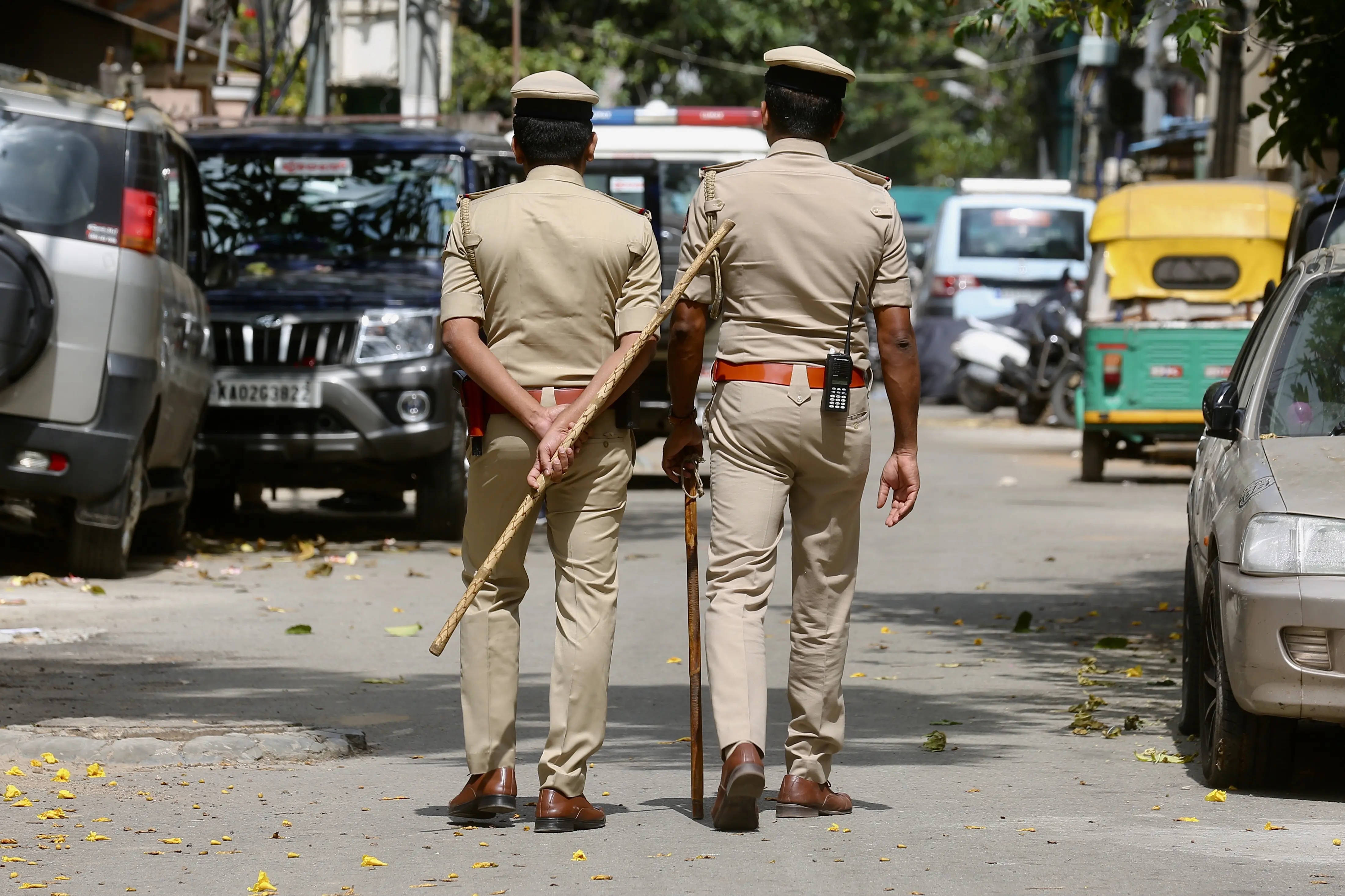 Indian 桌布 壁紙 — 兩名身穿卡其色制服的警察在一條陽光明媚的城市街道上走開，街道兩旁停滿了車，還有散落的黃葉。