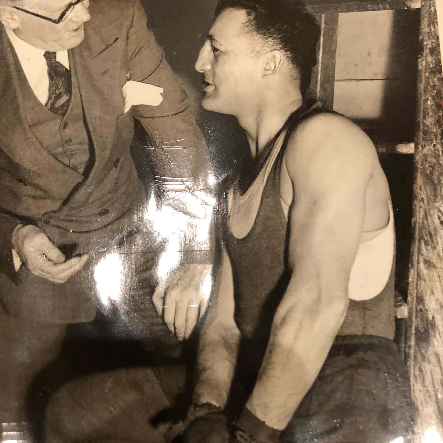 Boxing 桌布 壁紙 — 兩名身穿復古服裝的男子在光線昏暗、木牆和反光表面的房間內近距離交談。