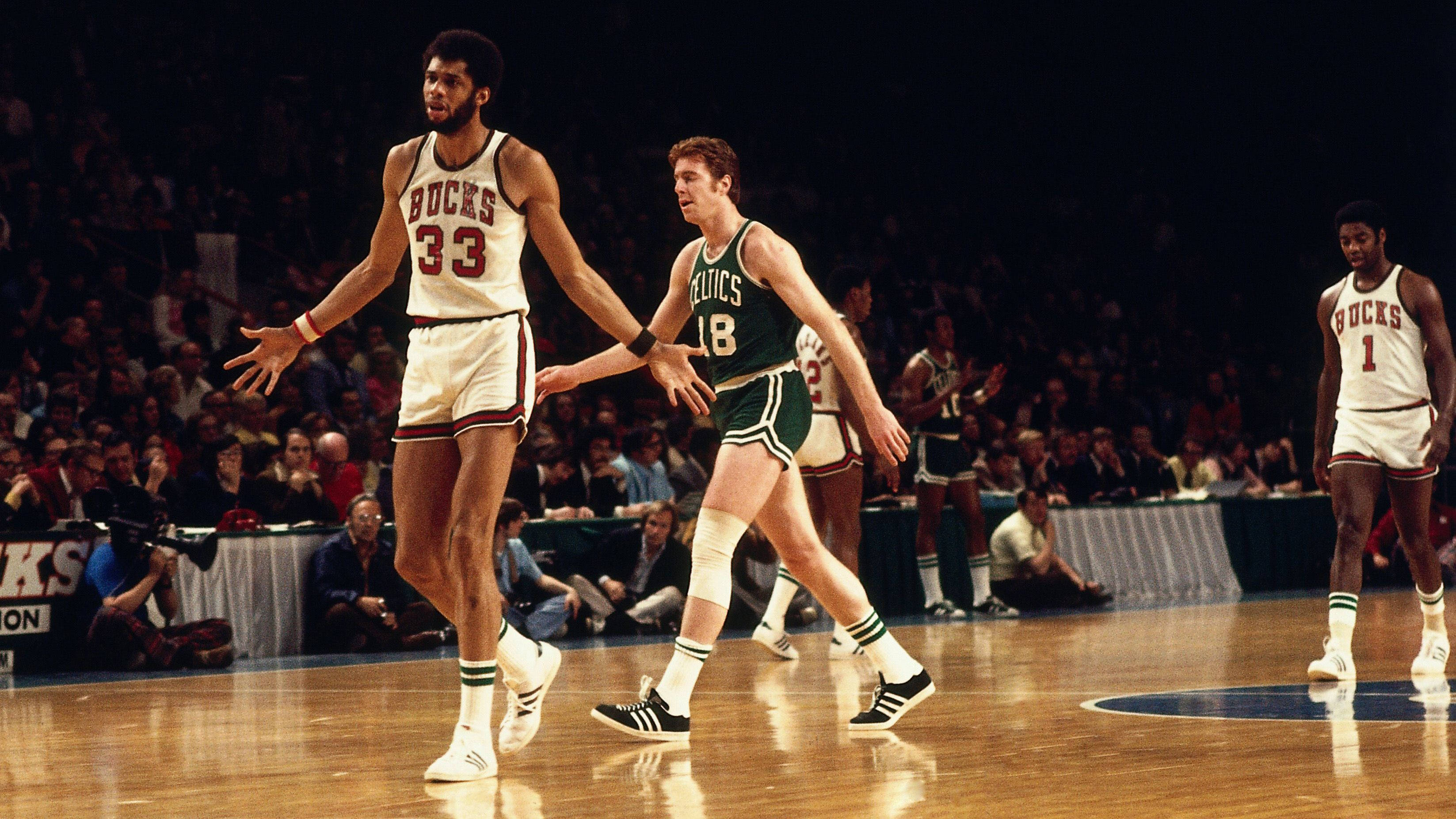 Kareem 桌布 壁紙 — 兩名身穿復古球衣的籃球運動員在明亮的場館燈光下，於拋光球場上激烈競爭。
