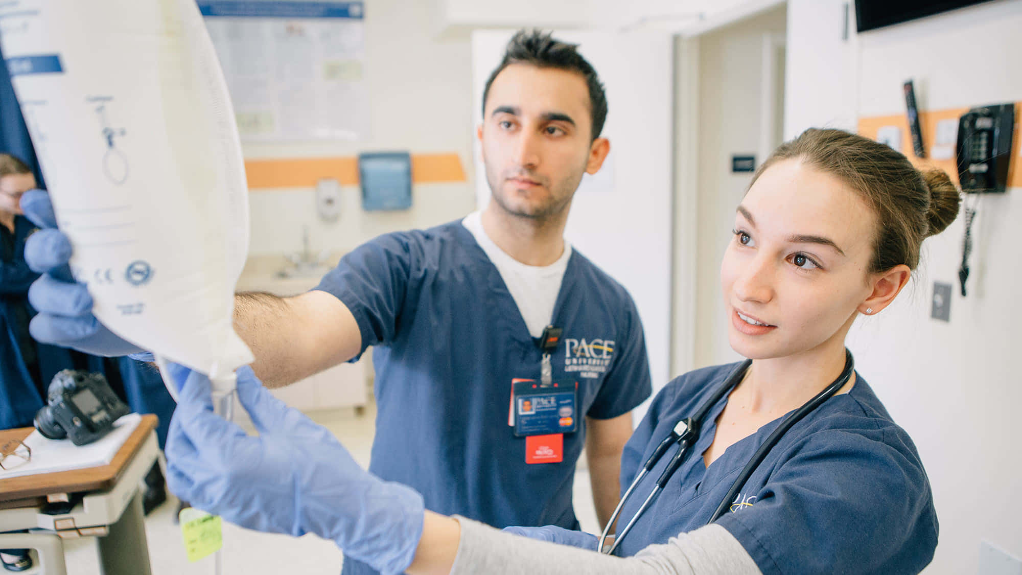 Nursing 桌布 壁紙 — 兩名身穿手術服的醫科學生在醫院房間內合作，一人拿著靜脈輸液袋，另一人專注觀察。
