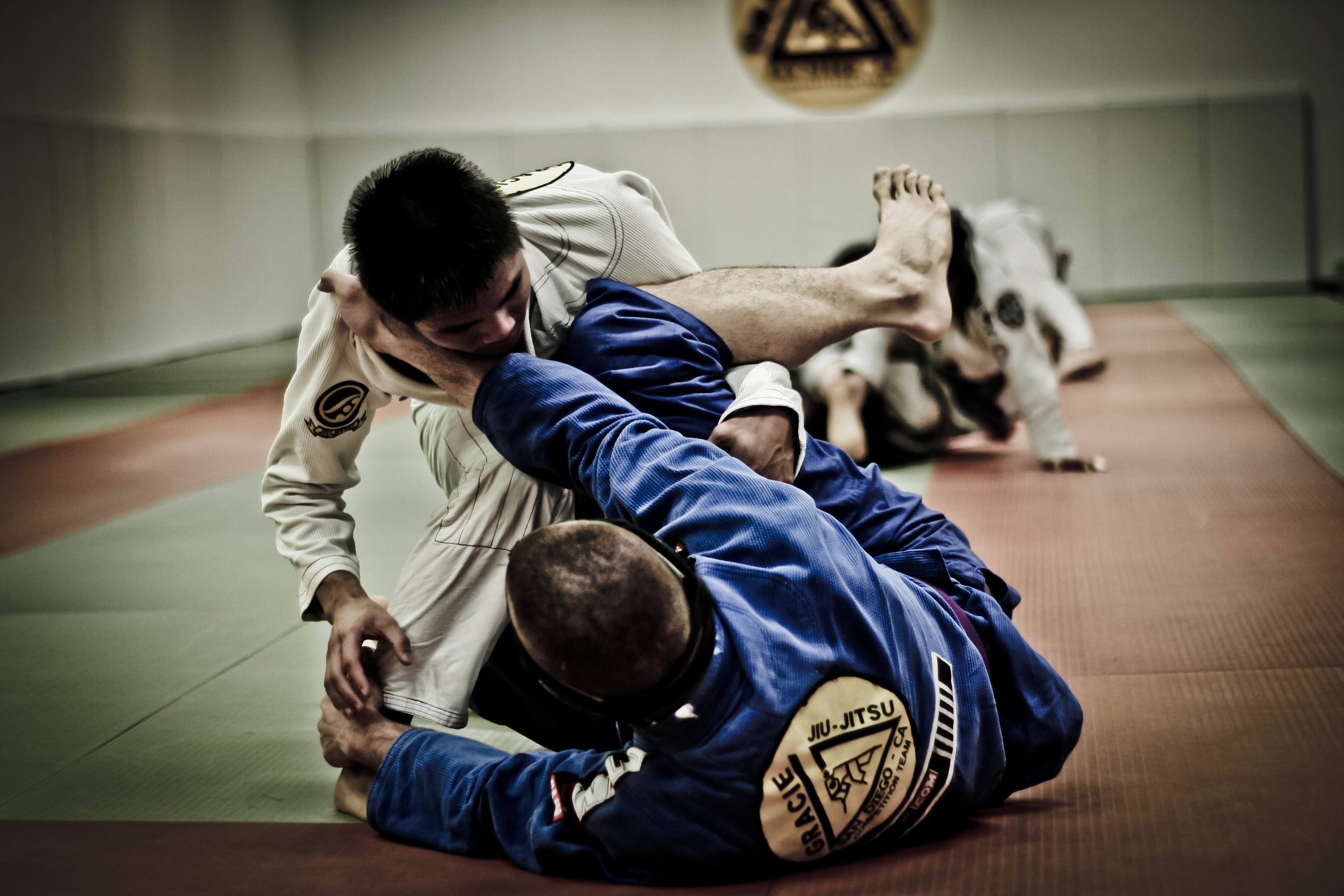 martial arts 桌布 壁紙 — 兩名身穿柔道服的男子在巴西柔術訓練期間在墊子上激烈纏鬥。