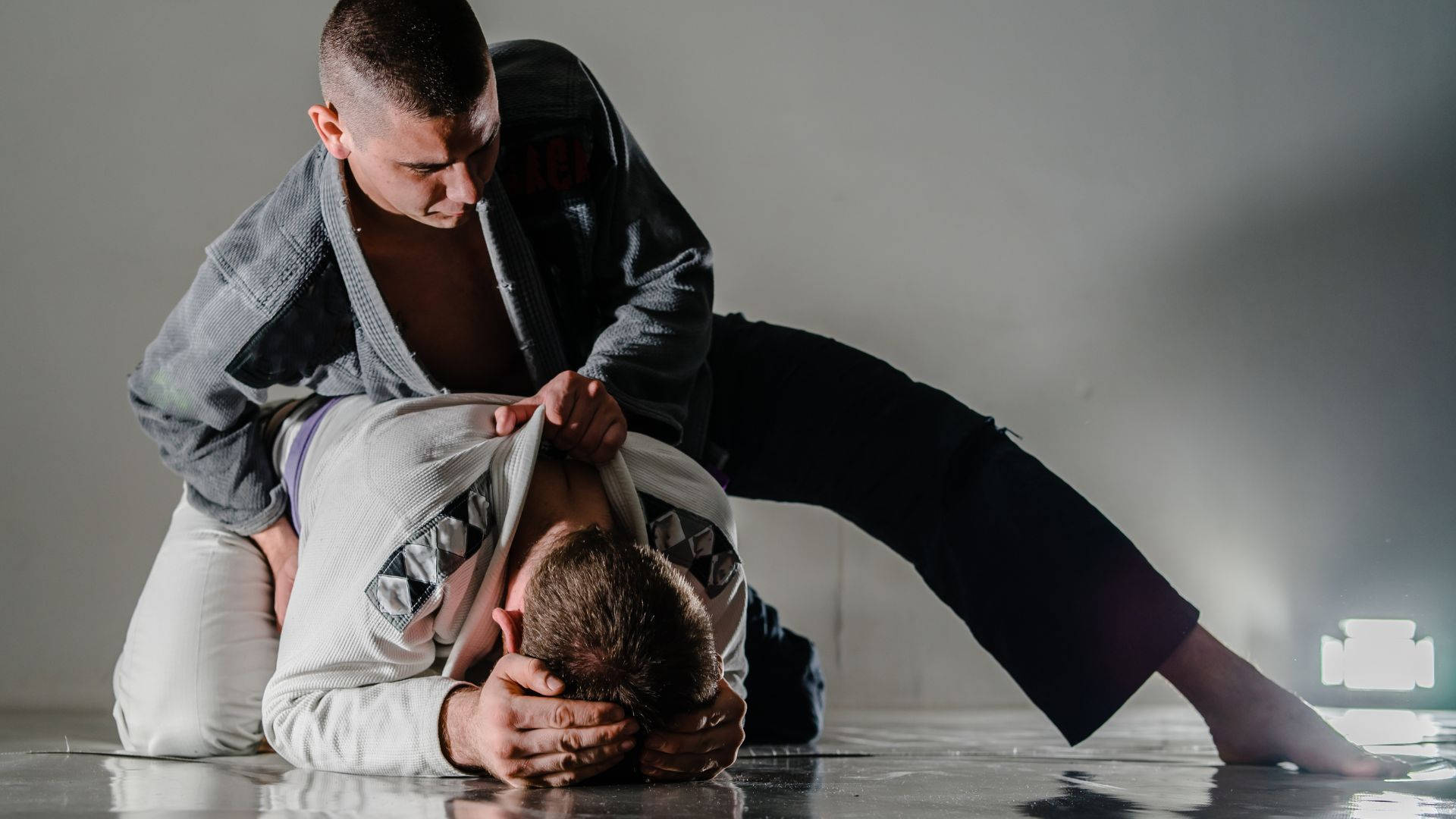 martial arts 桌布 壁紙 — 兩名身穿格鬥道服的男子在反射的錄音室地板上，於戲劇性燈光下執行一個動態的降服鎖技。