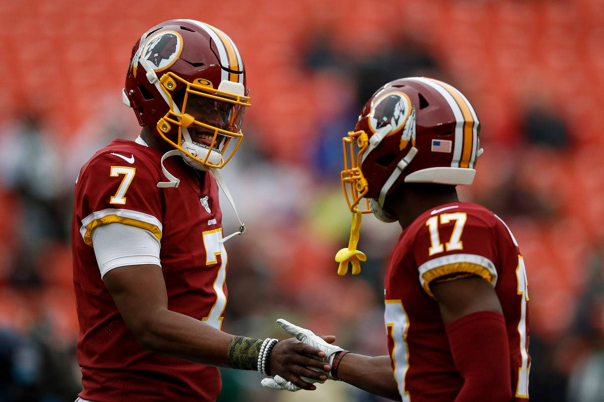 Football Players 桌布 壁紙 — 兩名身穿棗紅色頭盔和球衣的華盛頓美式足球隊球員在陽光明媚的體育場內握手。