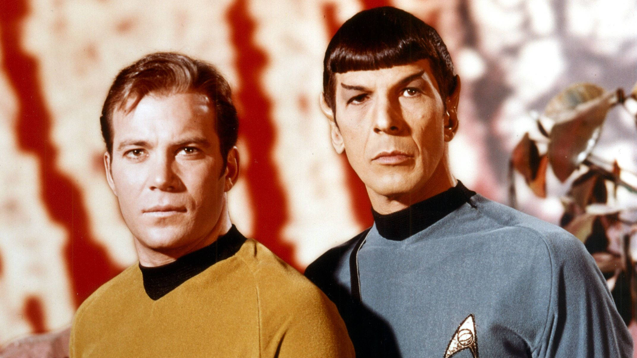 Spock 桌布 壁紙 — 兩名身穿標誌性制服的星際爭霸戰船員站在紅色和白色抽象背景前。
