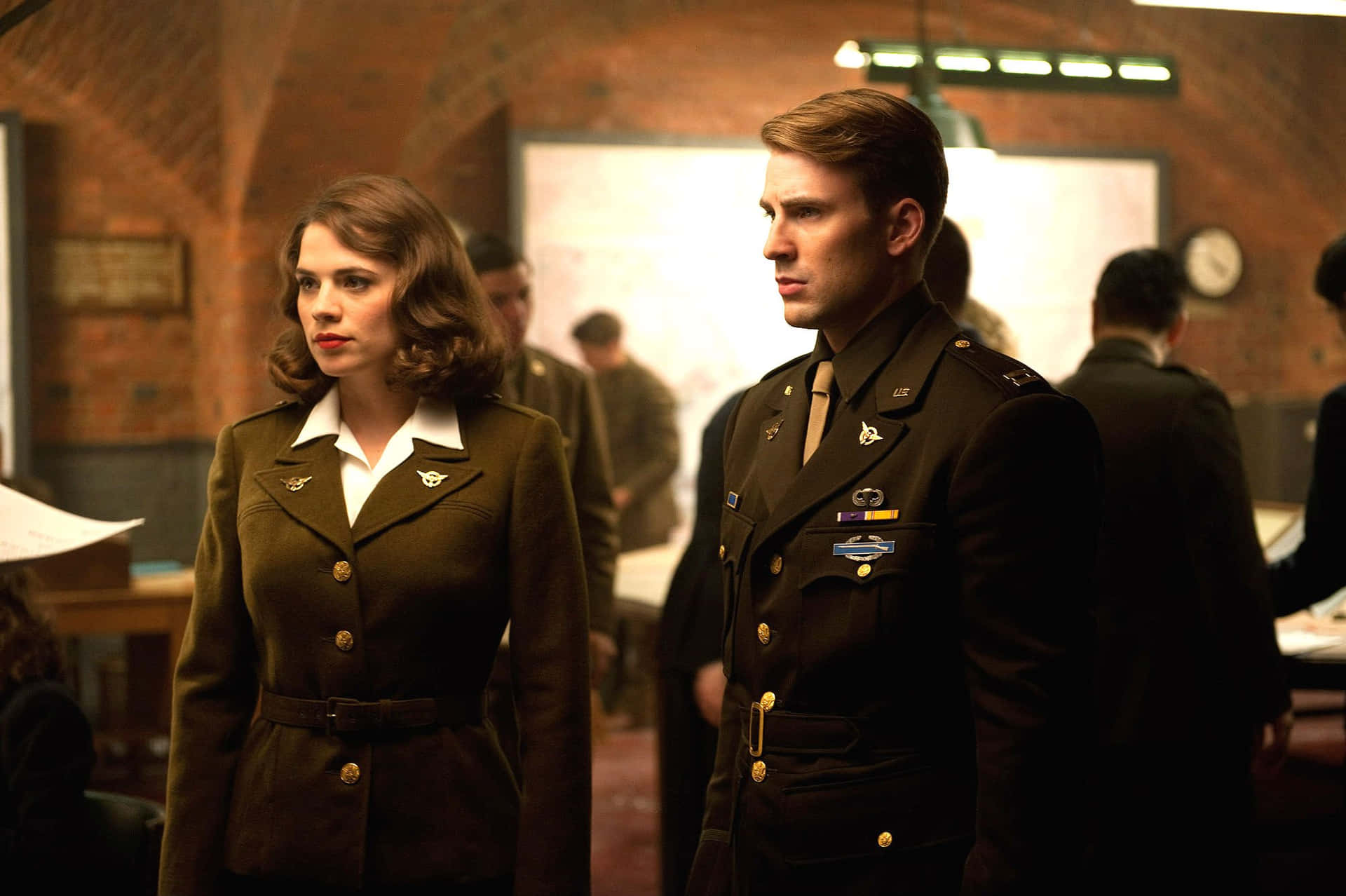 Peggy Carter 桌布 壁紙 — 兩名身穿橄欖色制服的士兵在磚牆的軍事事務所中莊嚴站立，背景有地圖和其他軍官。