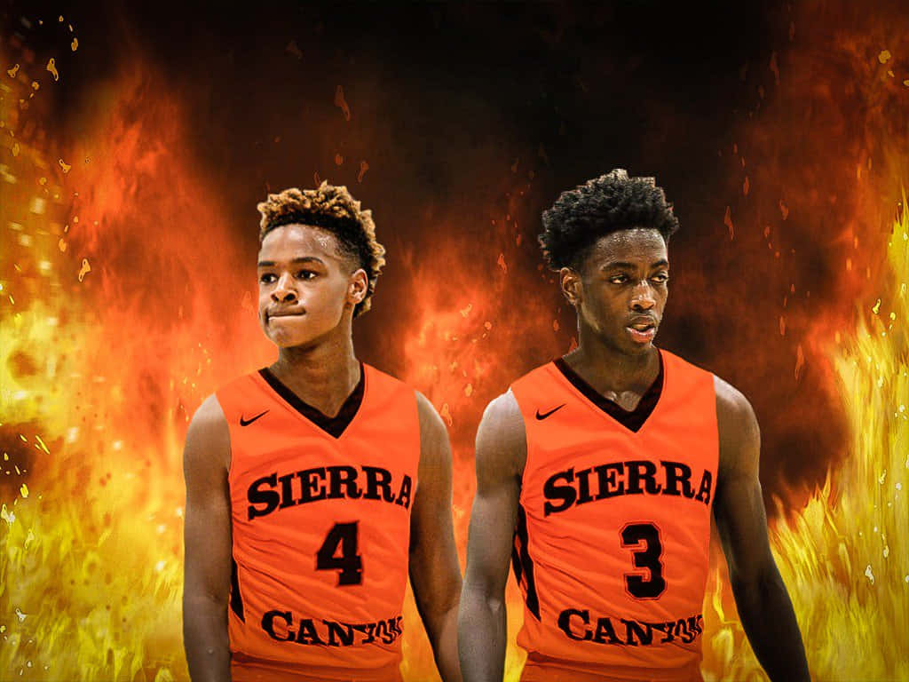 Bronny James 桌布 壁紙 — 兩名身穿橙色Sierra Canyon球衣的籃球運動員自信地站在充滿火焰和火花的熾熱背景前。