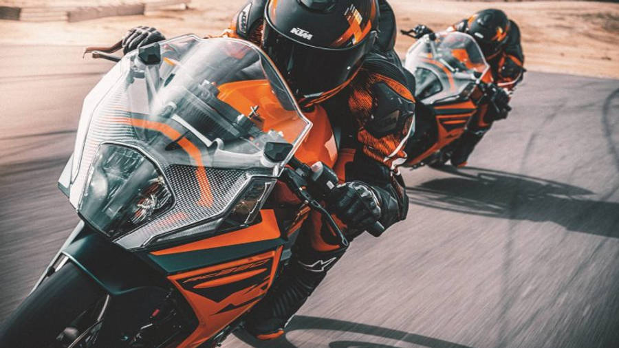 KTM RC 200 桌布 壁紙 — 兩名身穿橙色和黑色裝備的騎士，在陽光明媚的賽道上騎著高性能KTM摩托車傾斜入彎。