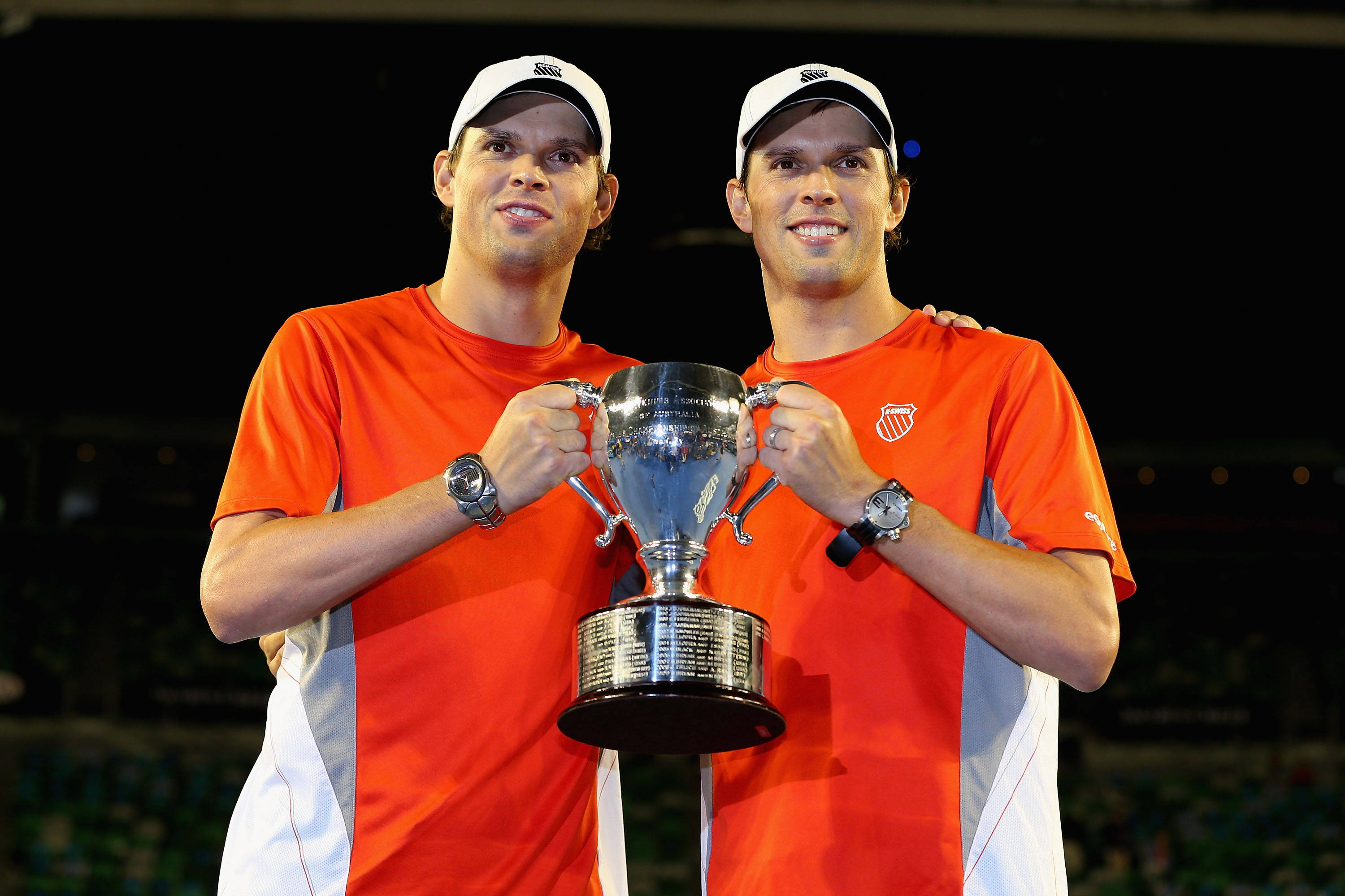 Tennis 桌布 壁紙 — 兩名身穿橙色球衣、面帶微笑的網球選手在體育場燈光下自豪地共同高舉一個大型銀色獎盃。