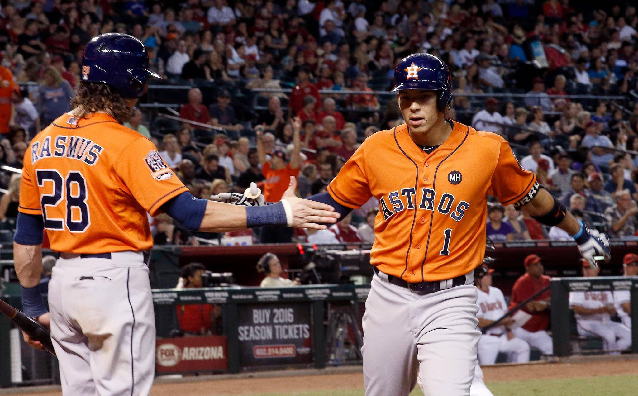 Carlos Correa 桌布 壁紙 — 兩名身穿橙色球衣的休士頓太空人棒球運動員在夜間比賽中，於燈光球場上擊掌，背景有歡呼的球迷。